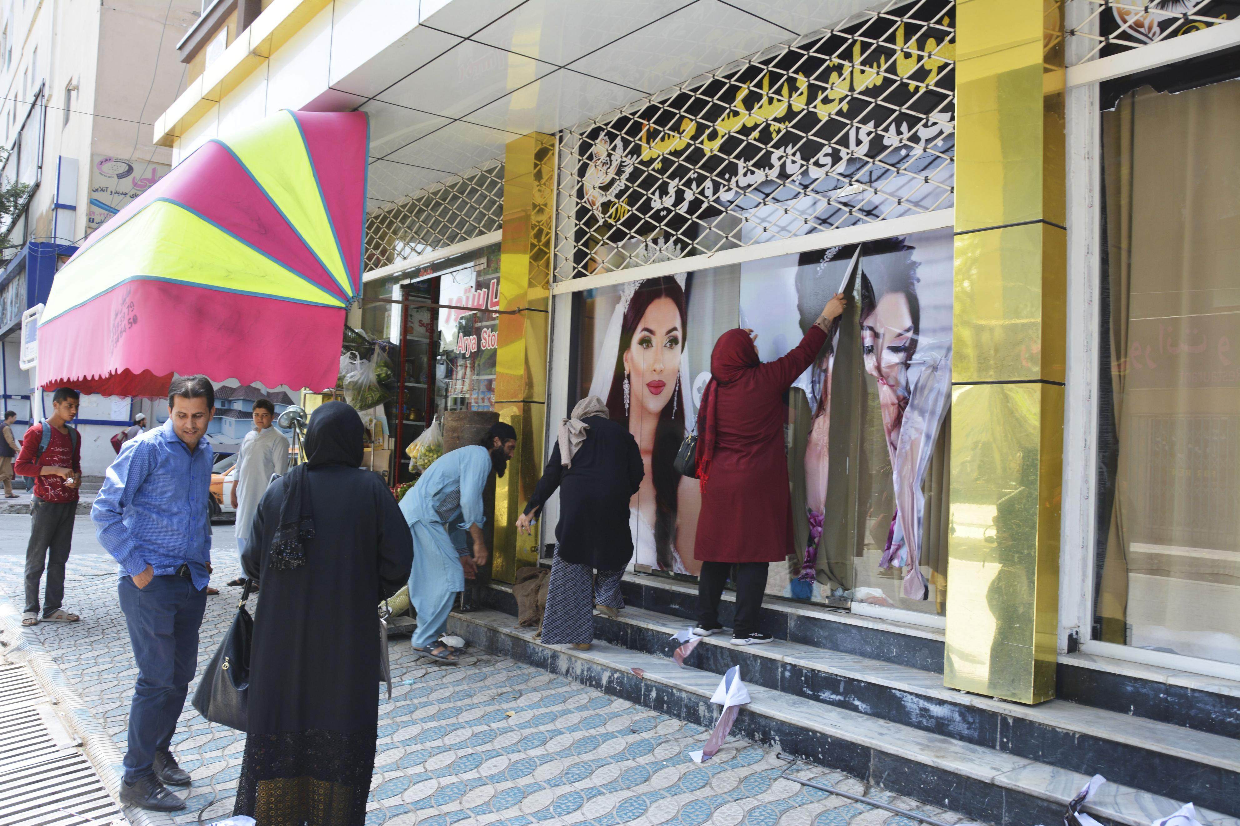 Workers at a beauty salon strip large images of women off the wall in Kabul on August 15 following news that the Taliban had swept into the Afghan capital. Photo: Kyodo