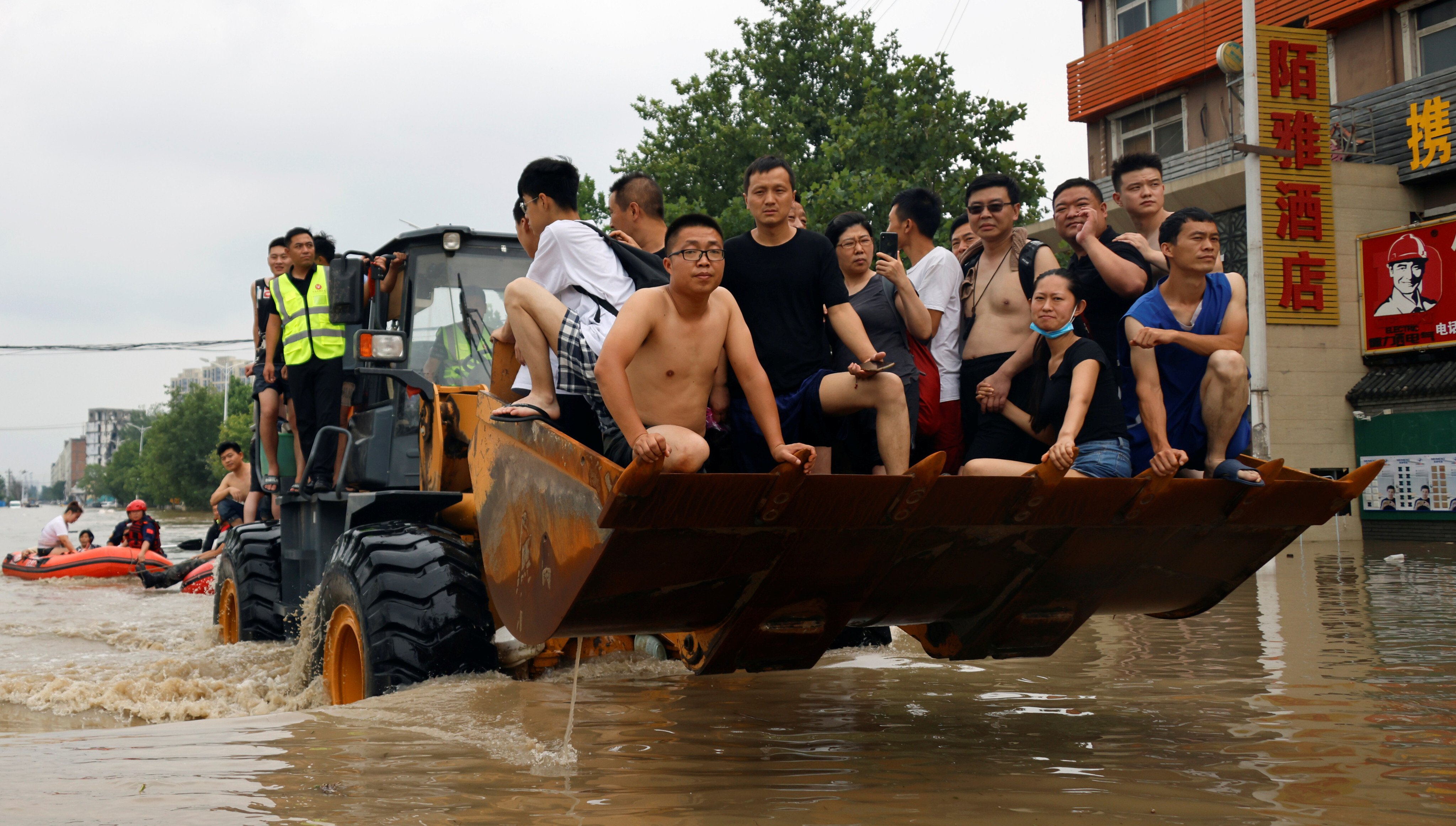 People ride a front loader as they make their way through a flooded road following heavy rainfall in Zhengzhou, Henan province, on July 22. Photo: Reuters
