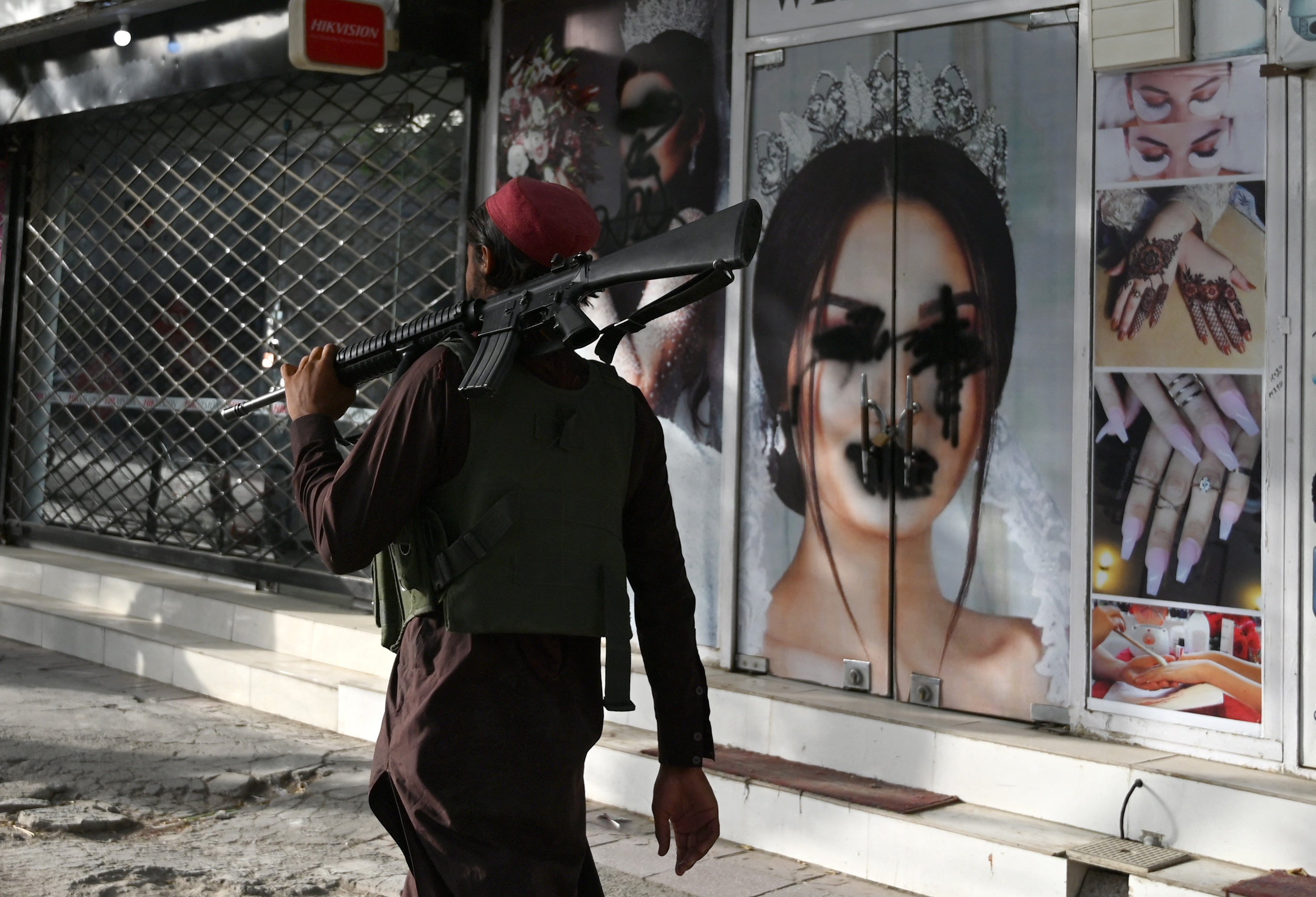 A Taliban fighter walks past a beauty salon with images of women defaced using spray paint in Shar-e-Naw, in Kabul, Afghanistan, on August 18. Photo: AFP