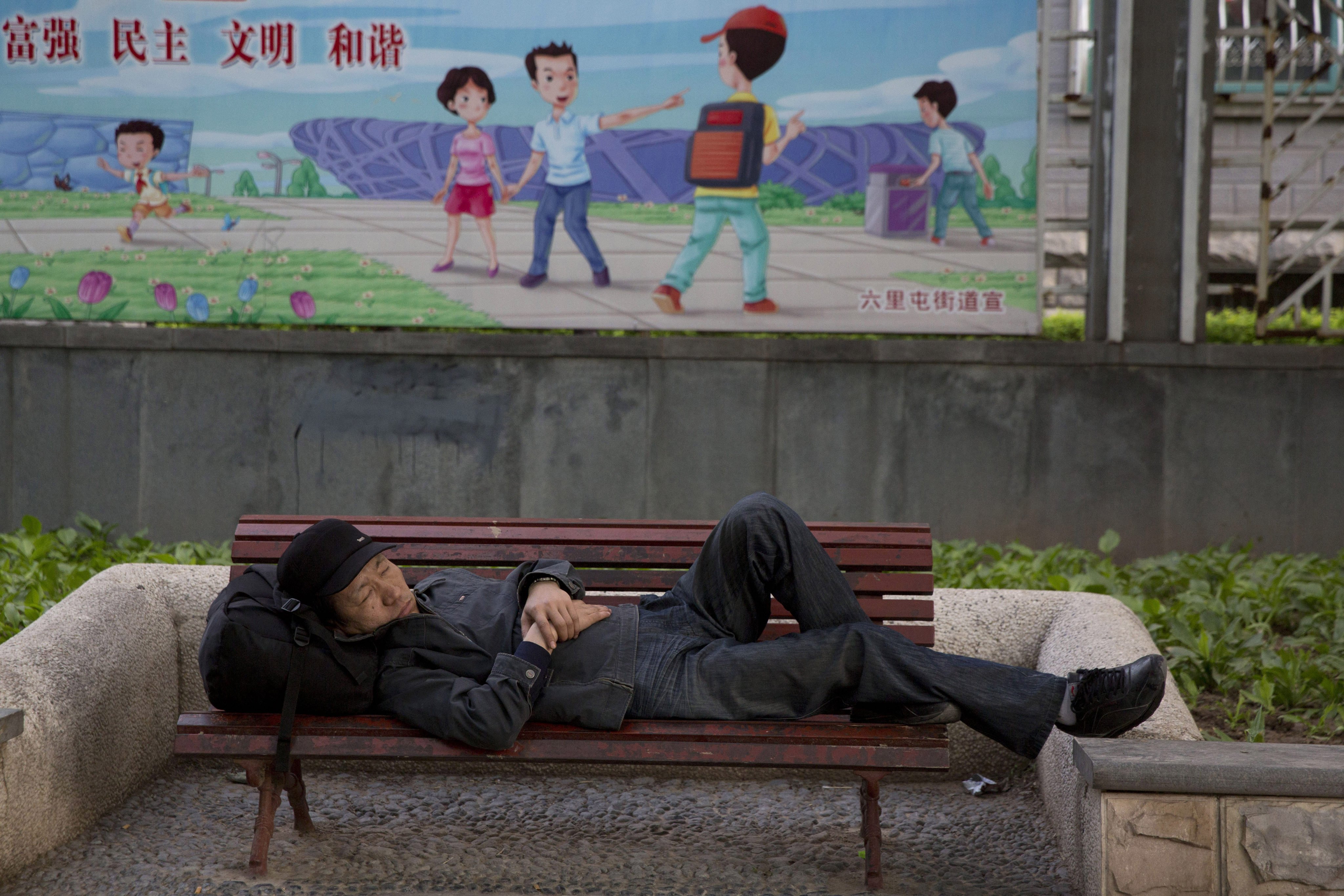 A man sleeps on a bench near a government billboard touting “prosperity, democracy, civilisation and harmony” on a street in Beijing on May 5, 2015. Photo: AP