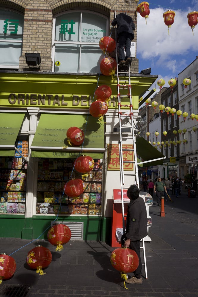 Two Chinese workmen work as a team attaching paper lanterns to a shop in London’s Chinatown. Photo: Getty Images