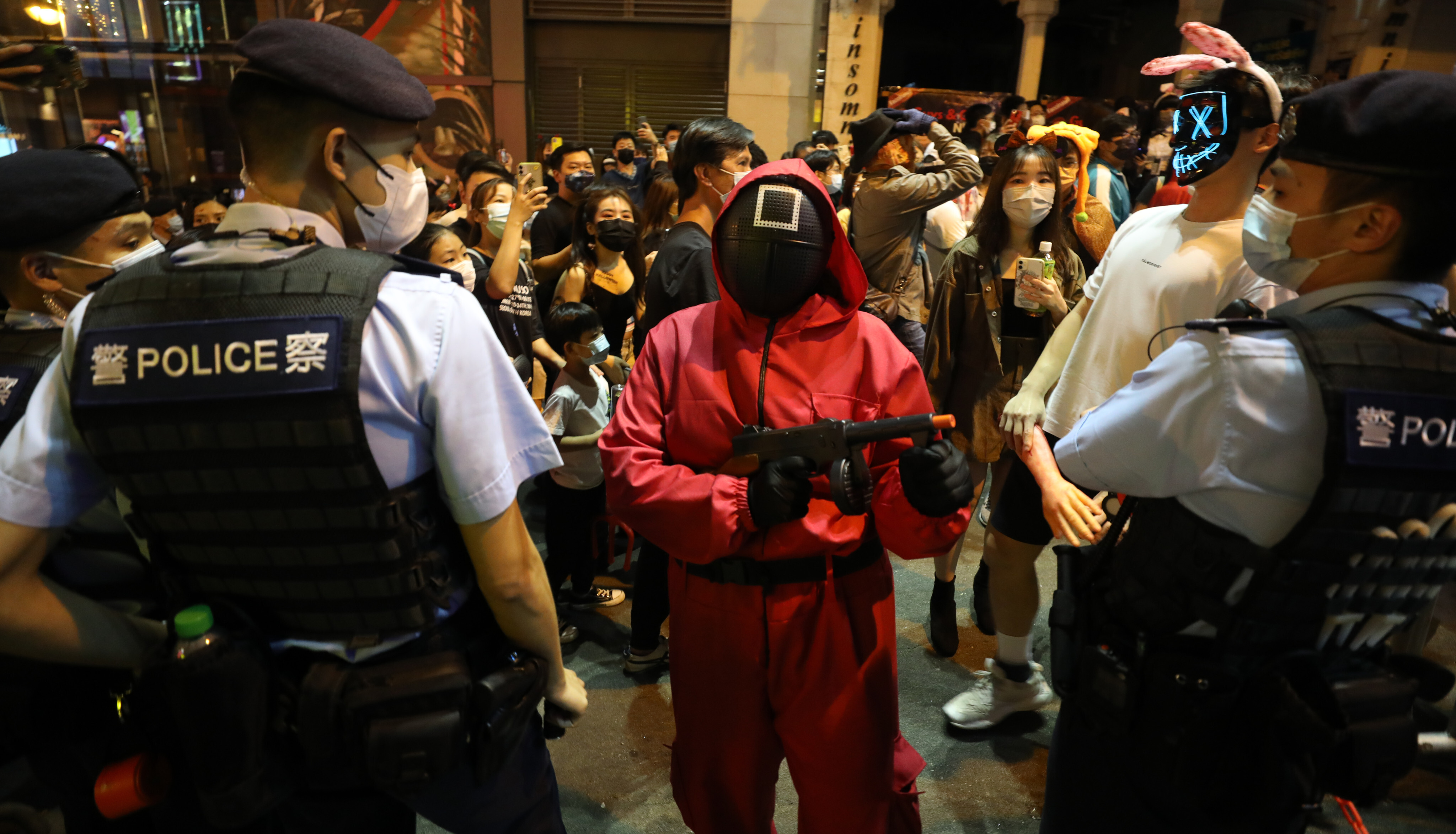 Halloween party-goers, one wearing a Squid Game square mask, stand next to police officers at Lan Kwai Fong in Central on October 31. Photo: Xiaomei Chen