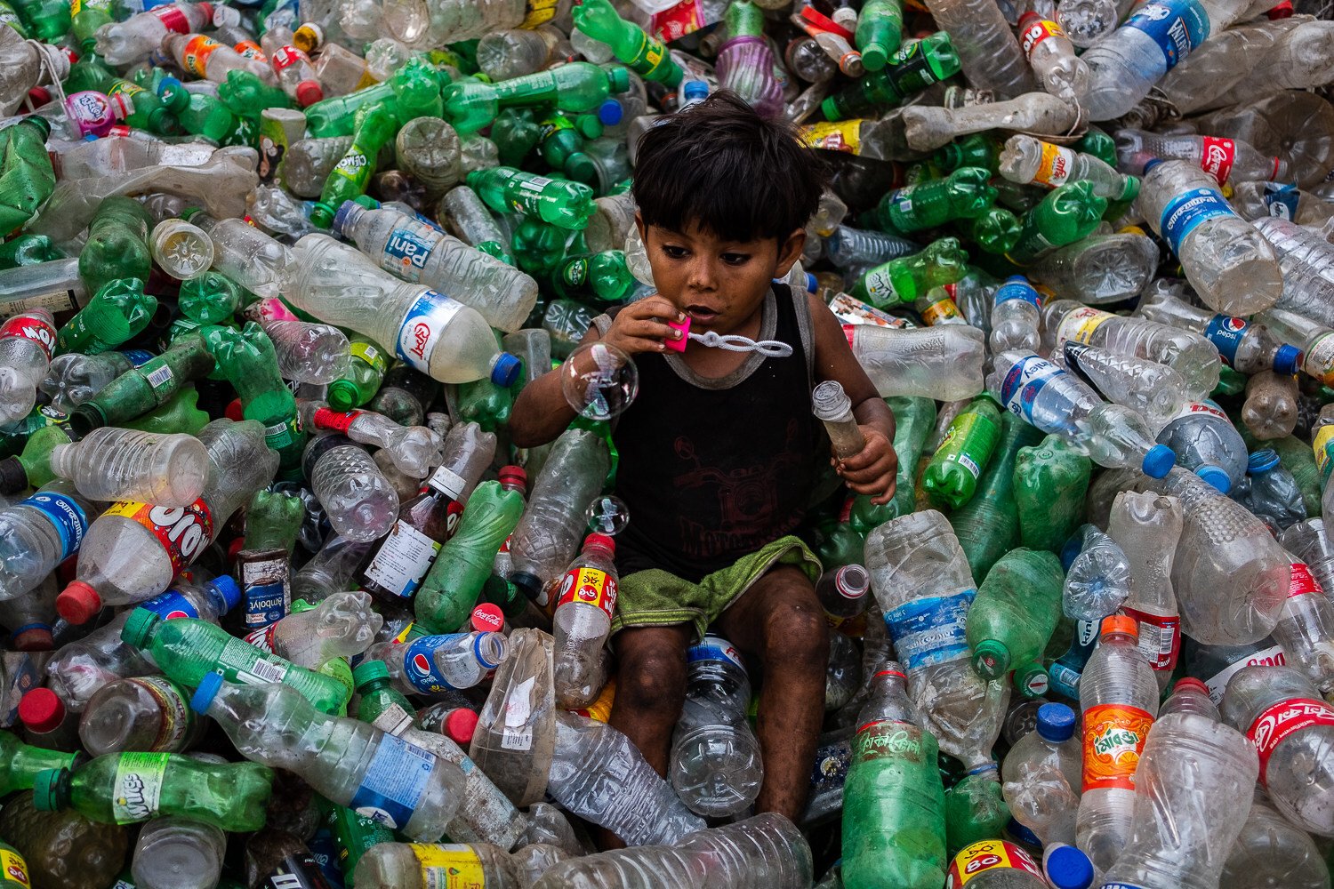 A boy plays with a bubble blower on a stack of plastic bottles inside a recycling factory in Dhaka, Bangladesh, on March 15. Photo: ZUMA Wire/dpa