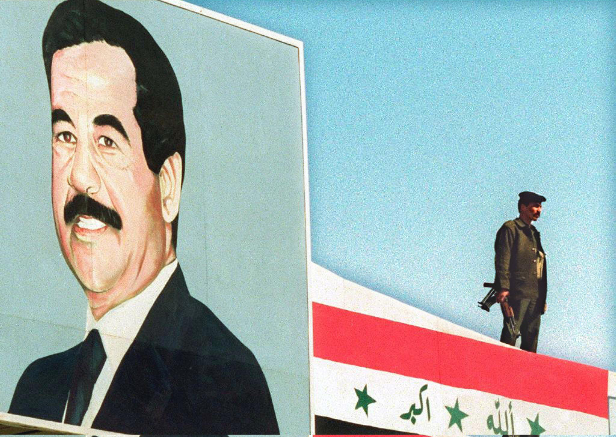 A soldier stands guard on top of a building draped with the Iraqi flag next to a portrait of President Saddam Hussein in Iraq in November 1997. Photo: AFP