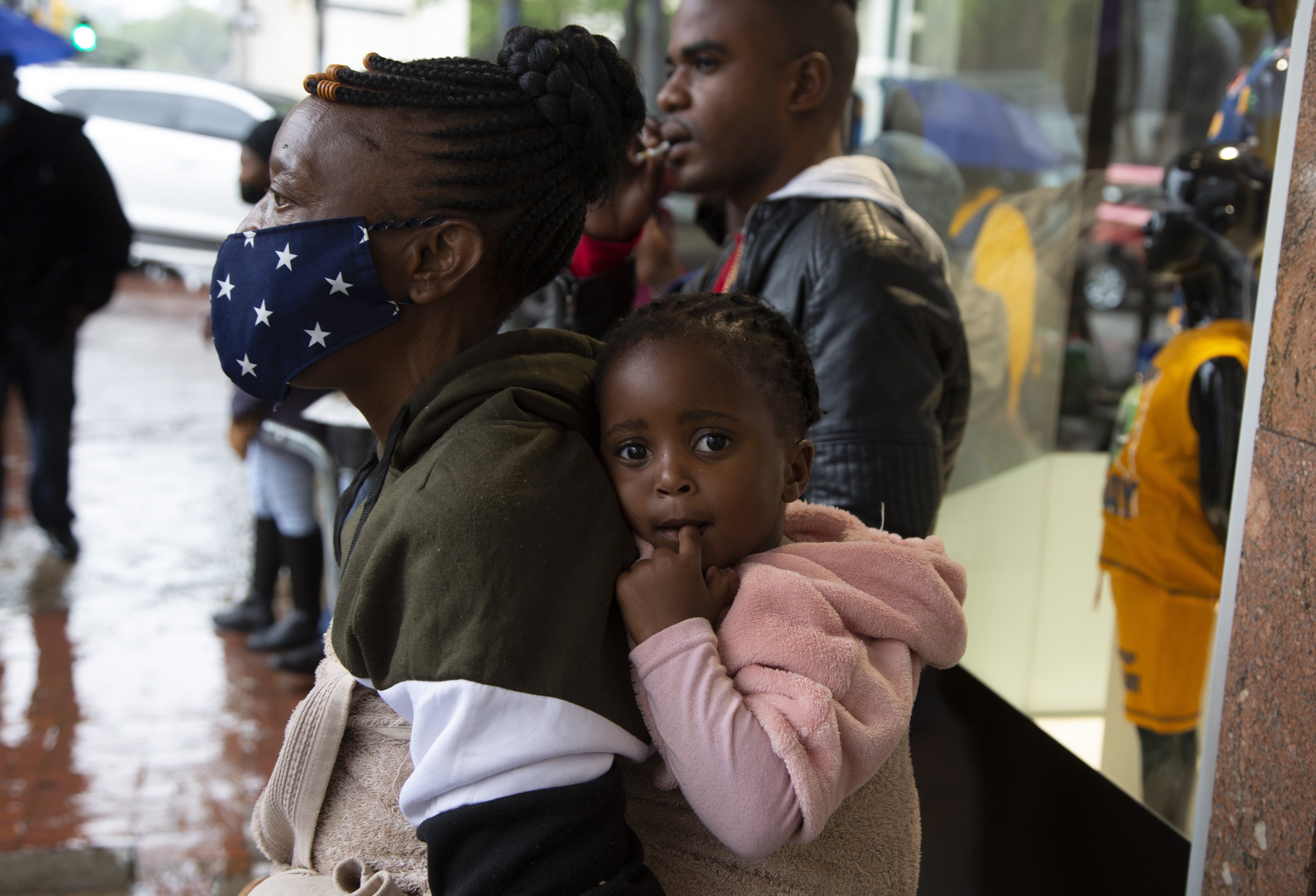 A woman wearing a face mask holds a child on her back on a crowded street in Pretoria, South Africa, on November 27. Photo: AP 