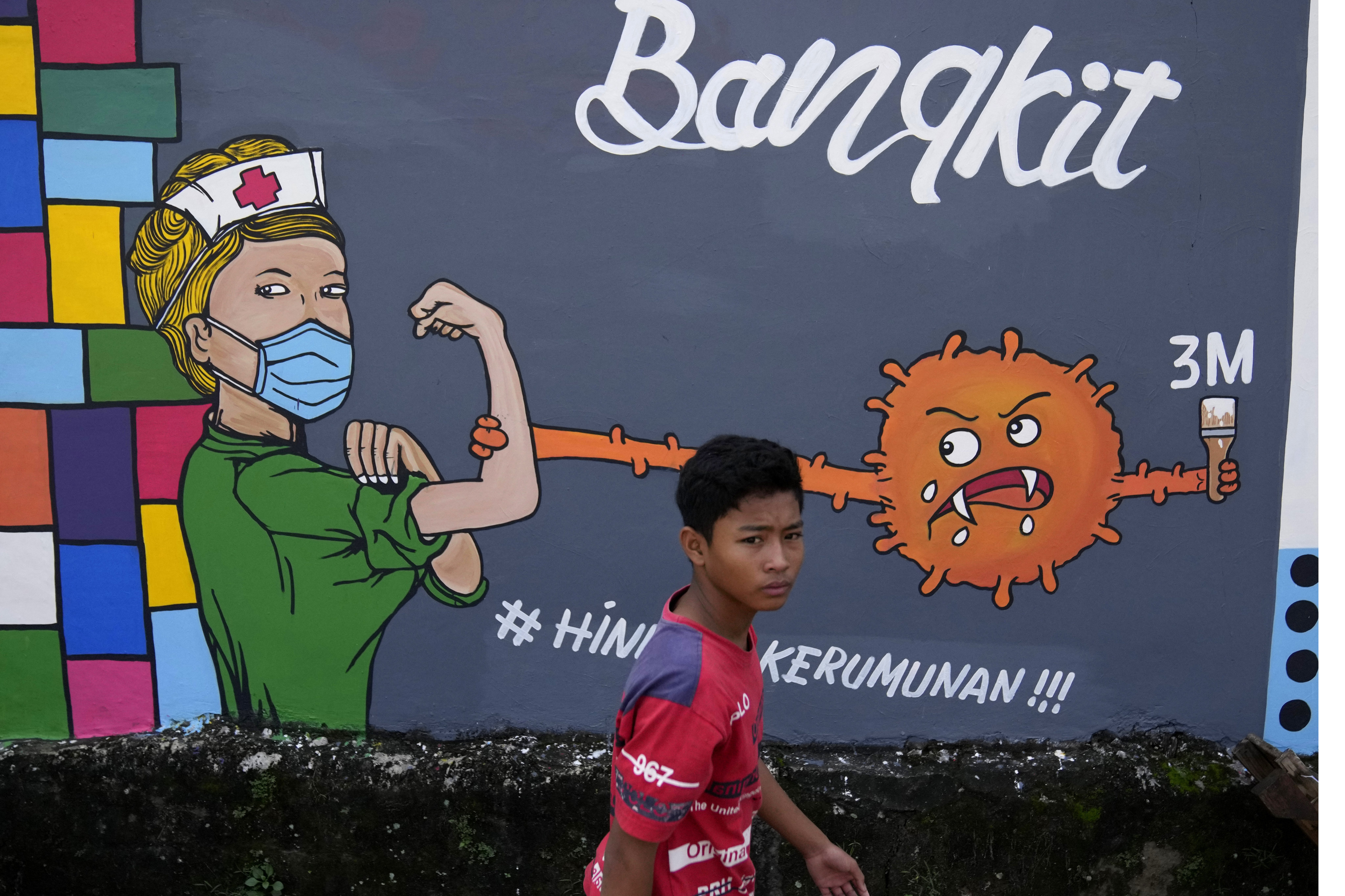 A young man walks past a coronavirus-themed mural honouring medical workers in Depok, on the outskirts of Jakarta, Indonesia, on June 25. Although global economic recovery continues, it is uneven, and the Omicron variant has heightened uncertainty. Photo: AP 