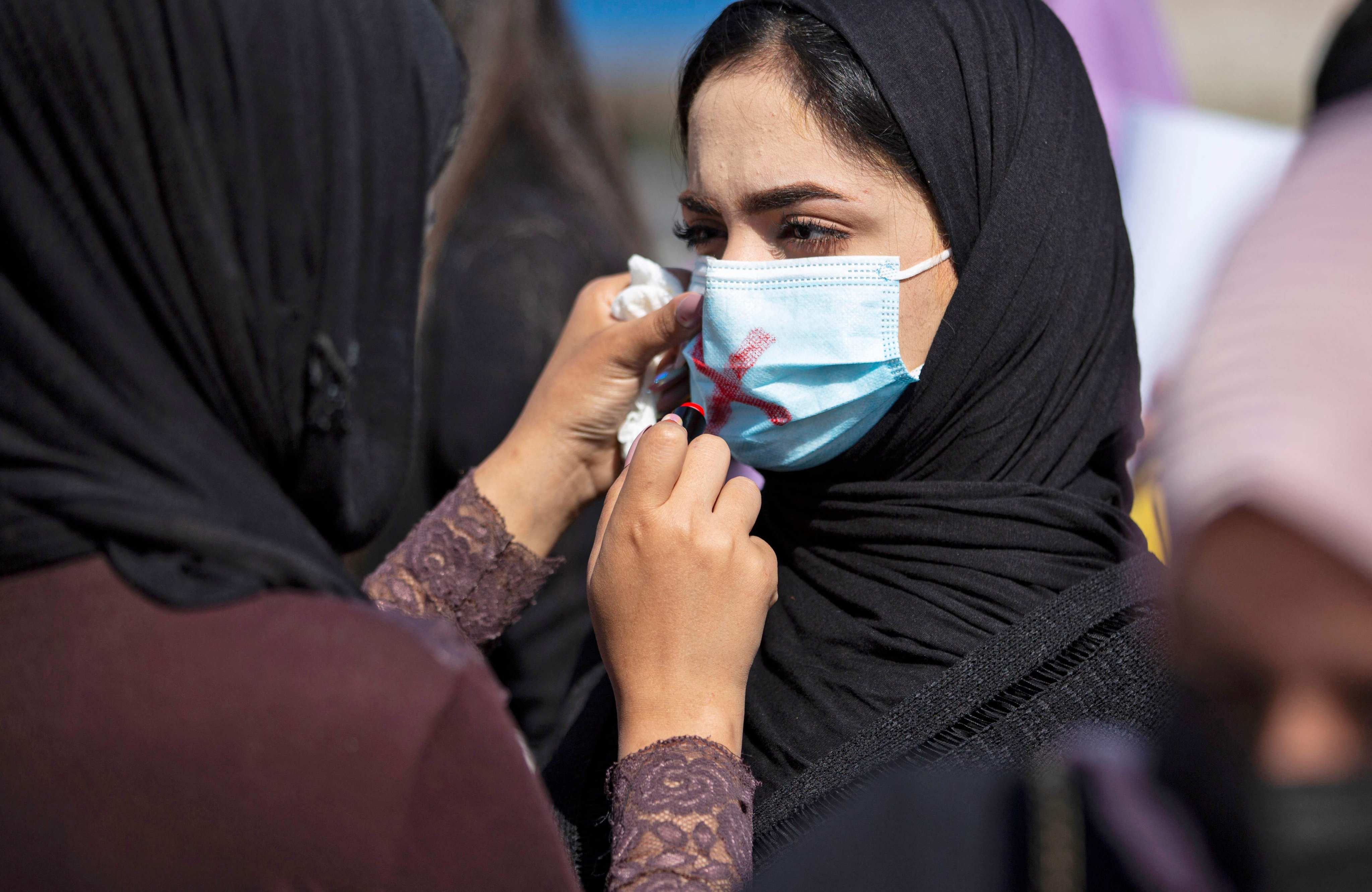 A demonstrator draws a cross on the mask of another protester as they attend a rally for International Women’s Day in Basra, Iraq, on March 8, 2021. Photo: AFP