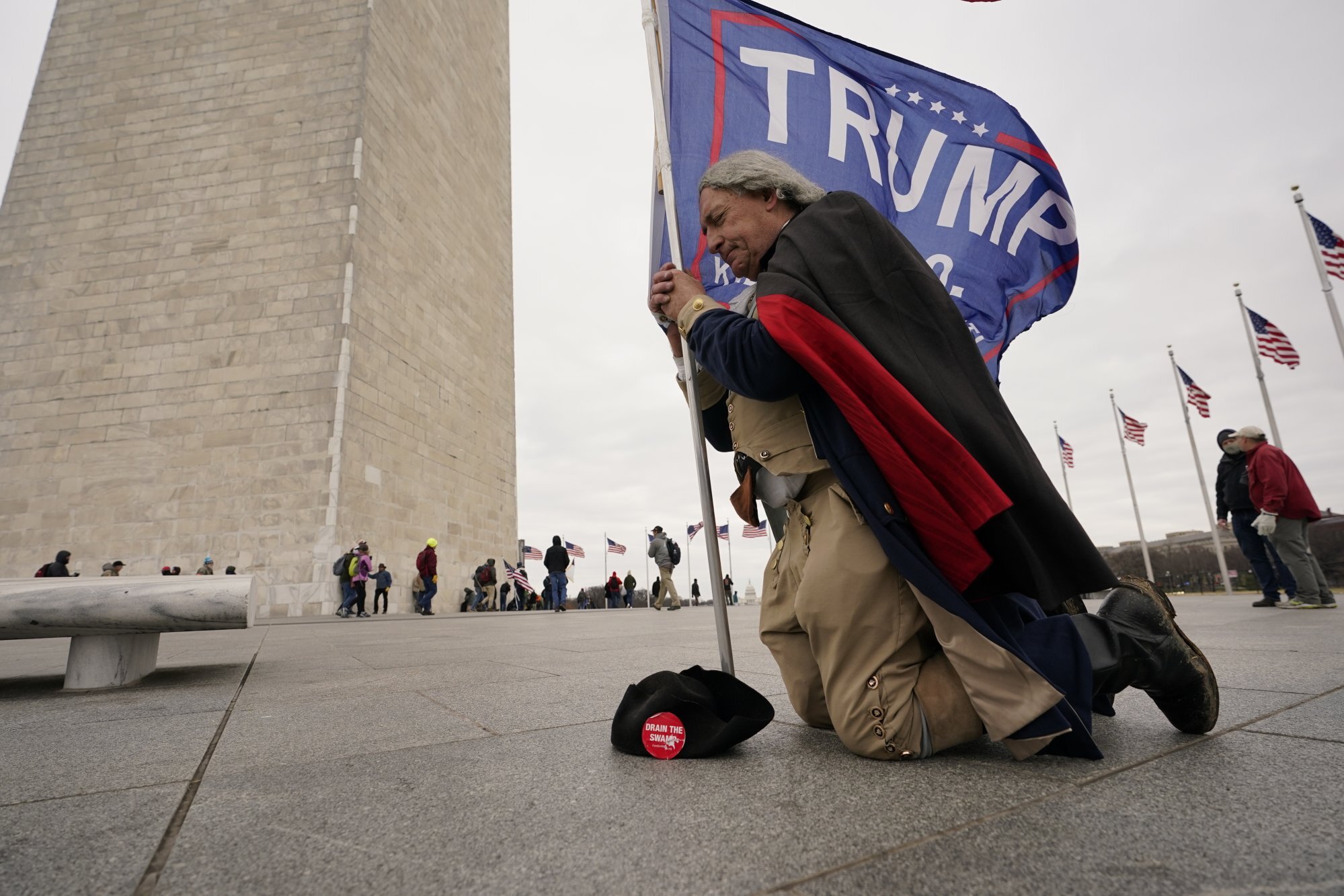 A man dressed as George Washington kneels and prays near the Washington Monument with a Donald Trump flag on January 6, 2021. Photo: AP