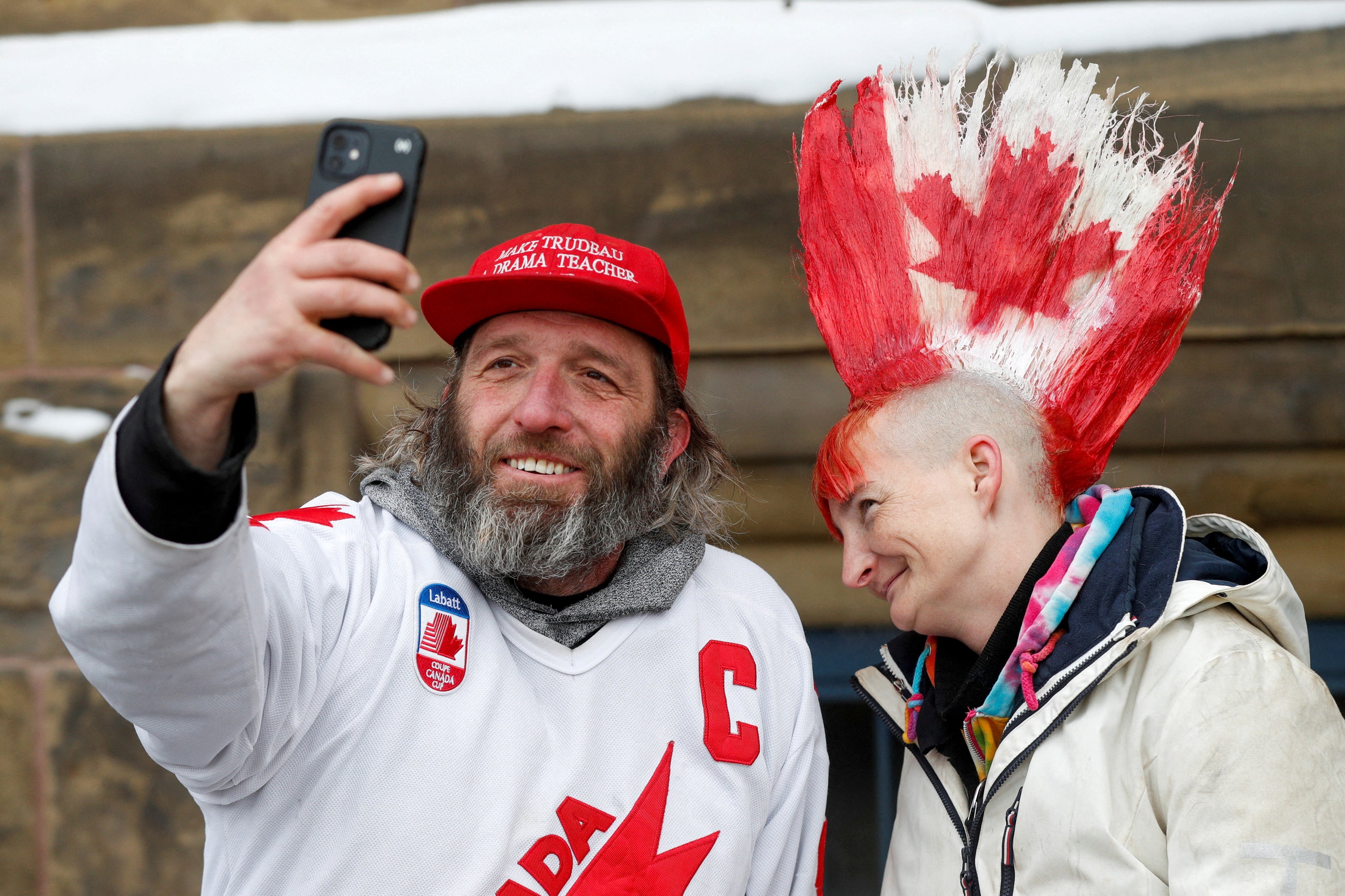 A man in a “Make Trudeau a drama teacher again” cap takes a selfie with a woman whose mohawk is painted with a Canadian maple leaf design, as truckers and supporters continue to protest against vaccine mandates, in Ottawa. Photo: Reuters