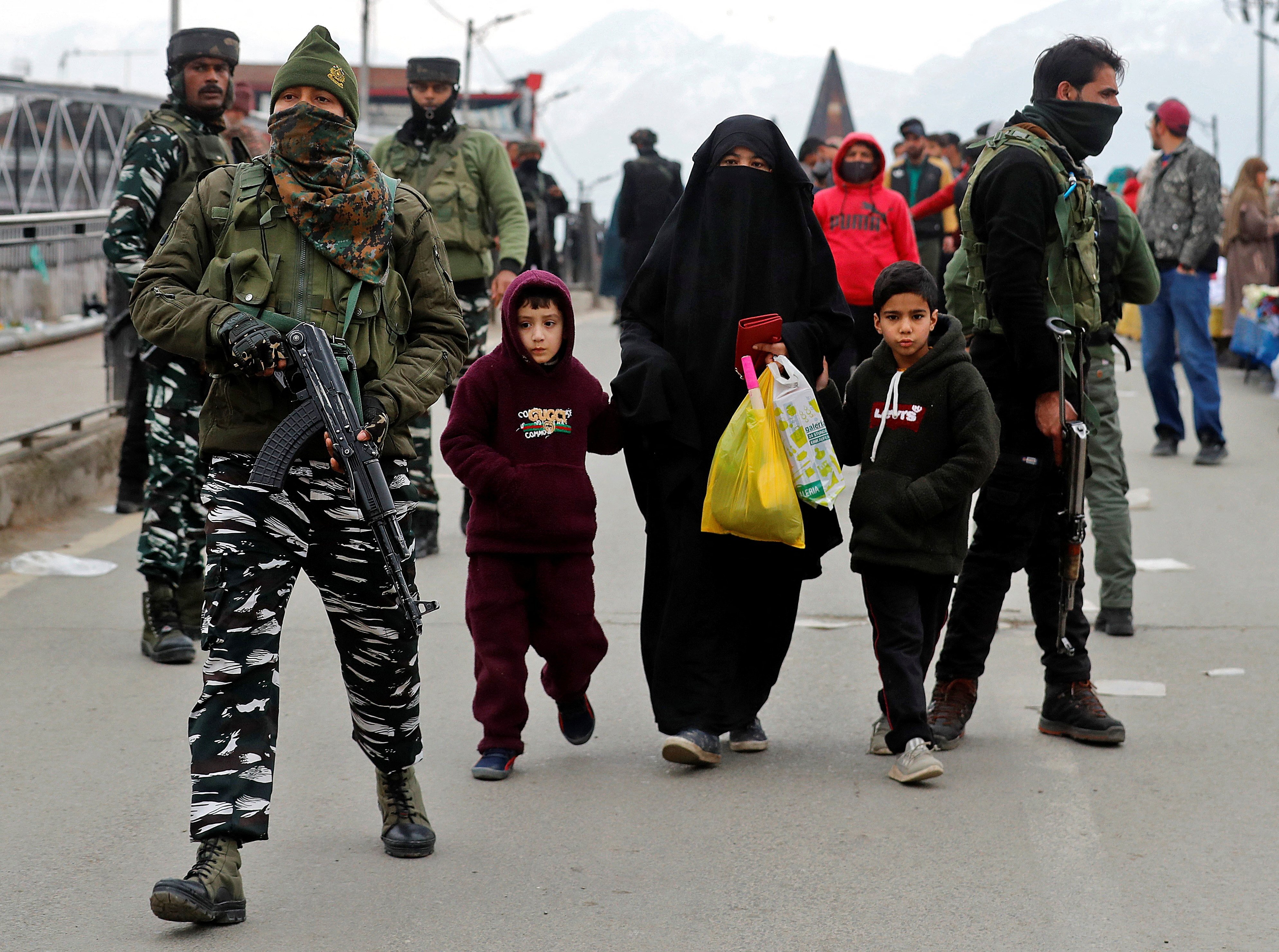 A veiled woman walks with her children past Indian security forces near the site of a grenade explosion in Srinagar, India on March 6. Photo: Reuters