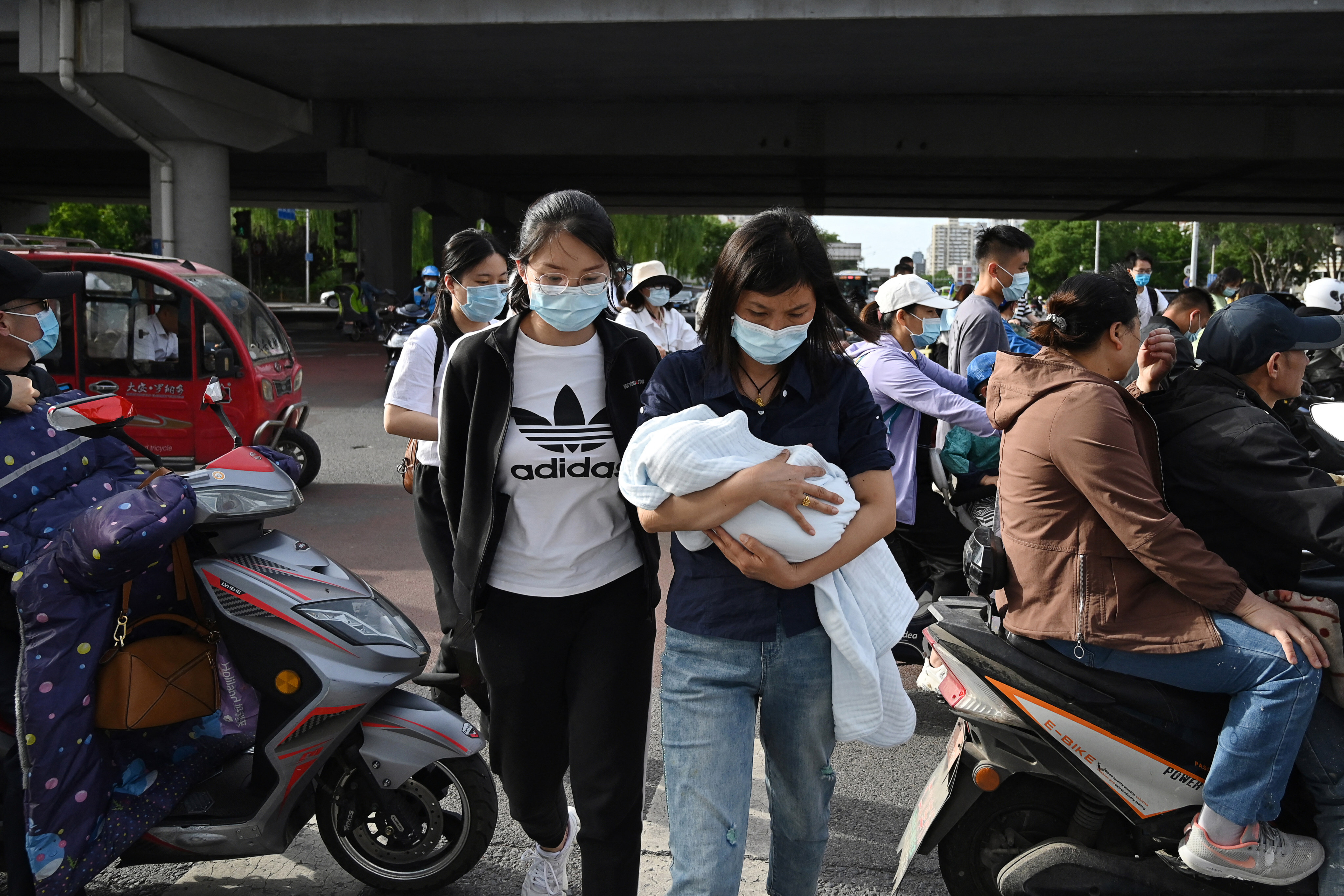 A woman carries a baby through a busy intersection in Beijing on June 2, 2021, days after China announced it would allow couples to have three children. Photo: AFP