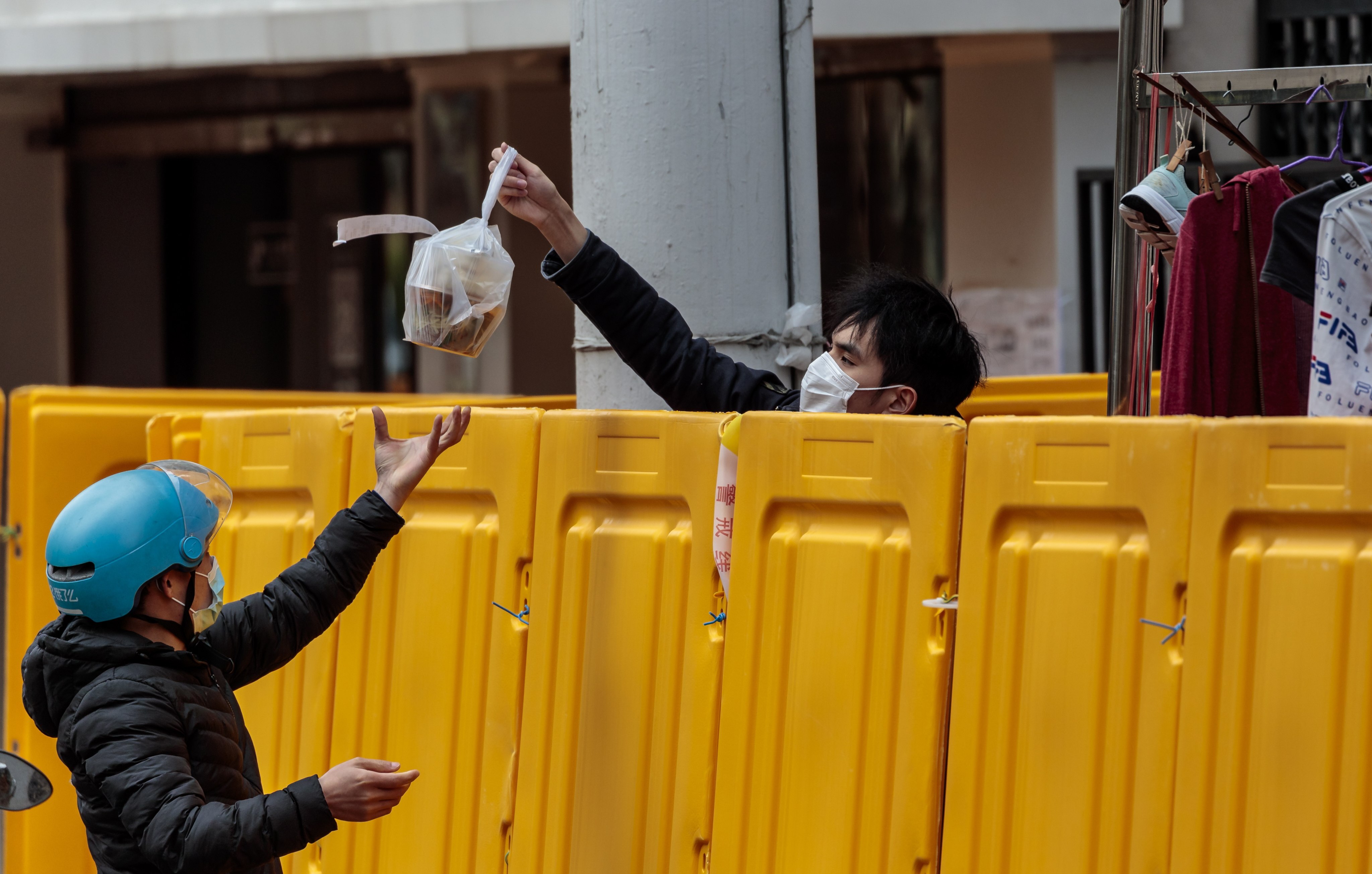 An Ele.me delivery courier passes ordered food, wrapped in a plastic bag, over the fence to a man under quarantine in Shanghai on March 28, 2022. Photo: EPA-EFE