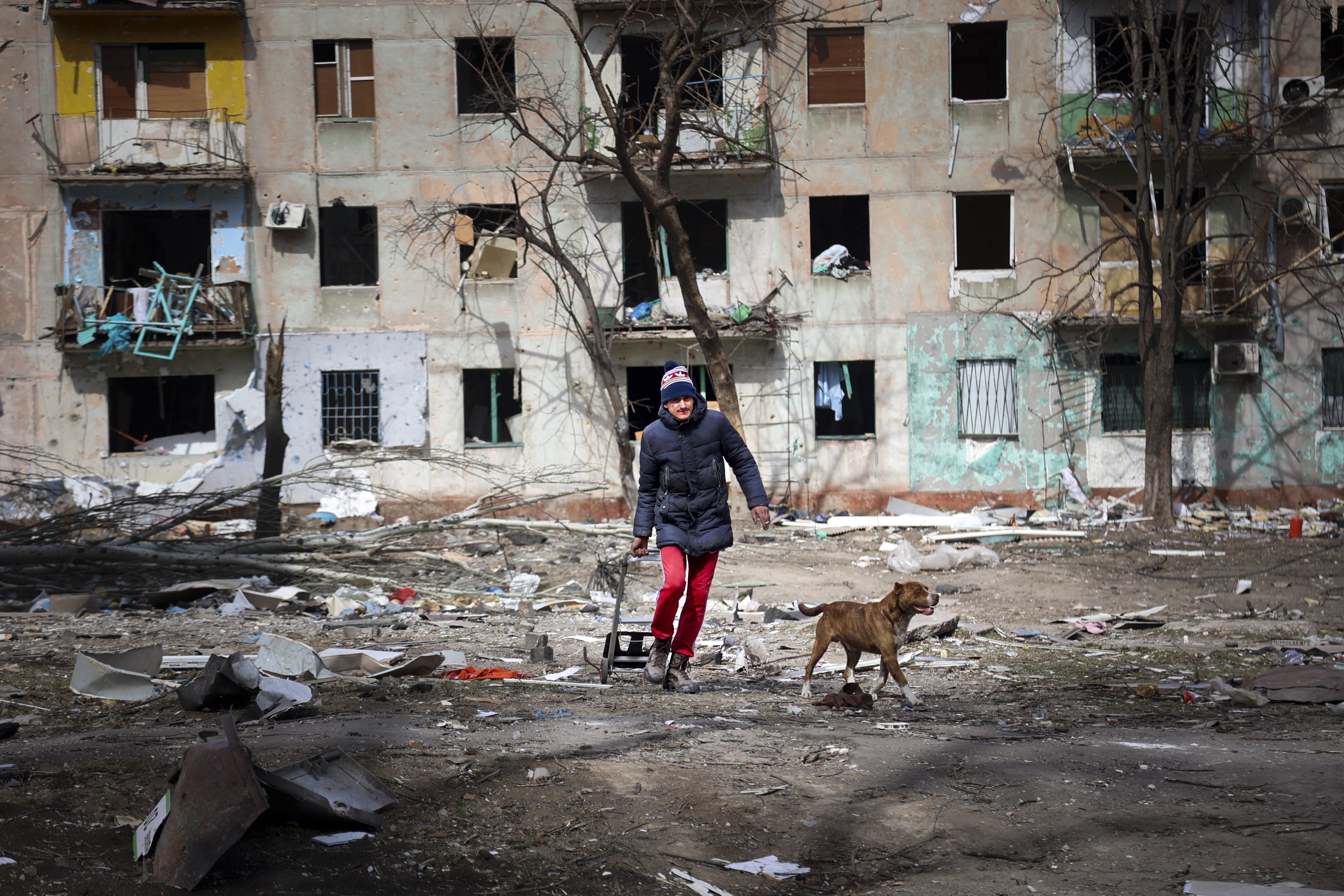 A man walks with his dog near a block of flats damaged by shelling from fighting on the outskirts of Mariupol, Ukraine, on March 29. Russia’s invasion of Ukraine has pushed Covid-19 out of the spotlight in many parts of the world, but the pandemic and government responses to it still have a large role to play in the global economy. Photo: AP