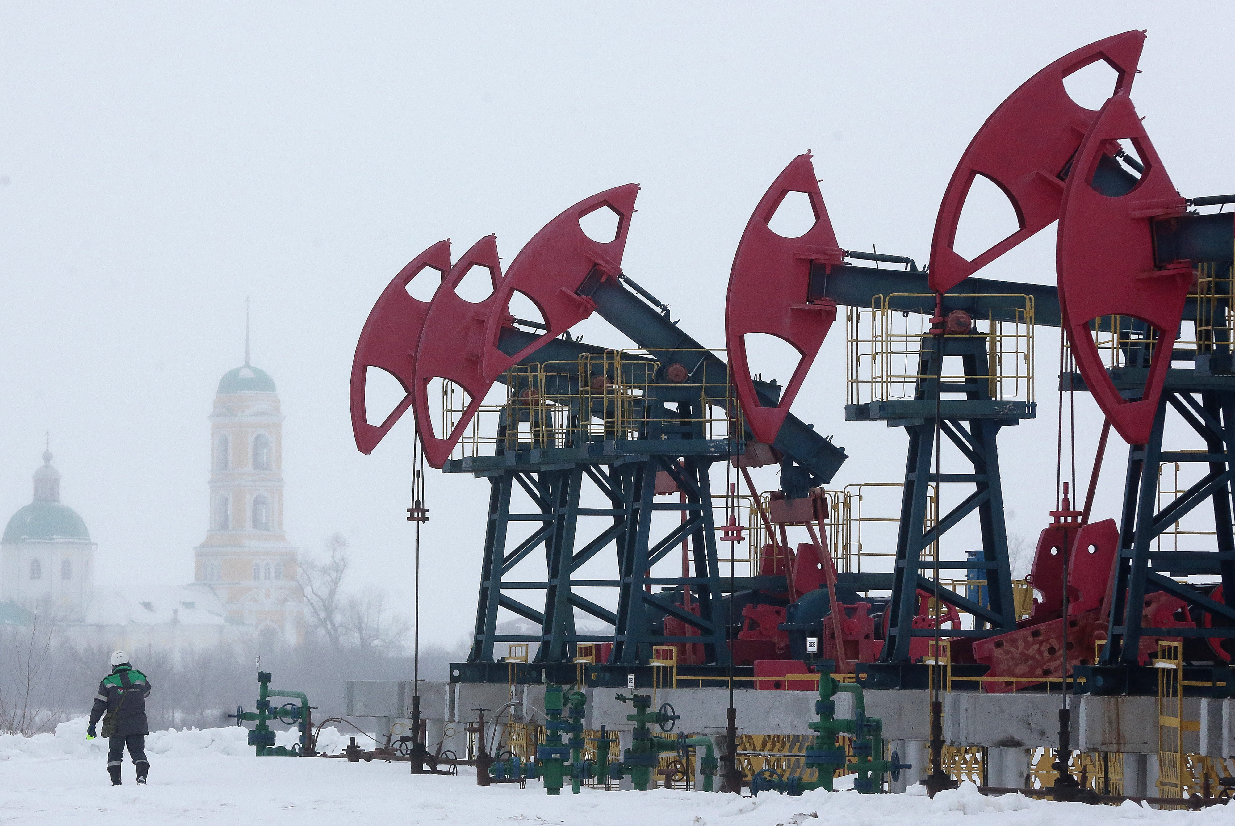 A worker passes a line of oil pumping jacks, also known as nodding donkeys, in the Bashneft PAO oilfield outside the village of Nikolo-Beryozovka near Neftekamsk, Russia, on Thursday, March 3, 2016. Bashneft is an upstream and down stream oil & gas provider which explores, produces and refines its own oil and gas which it extracts from brownfield reserves in the Russian Federation. Photographer: Andrey Rudakov/Bloomberg ORG XMIT: 608301091
