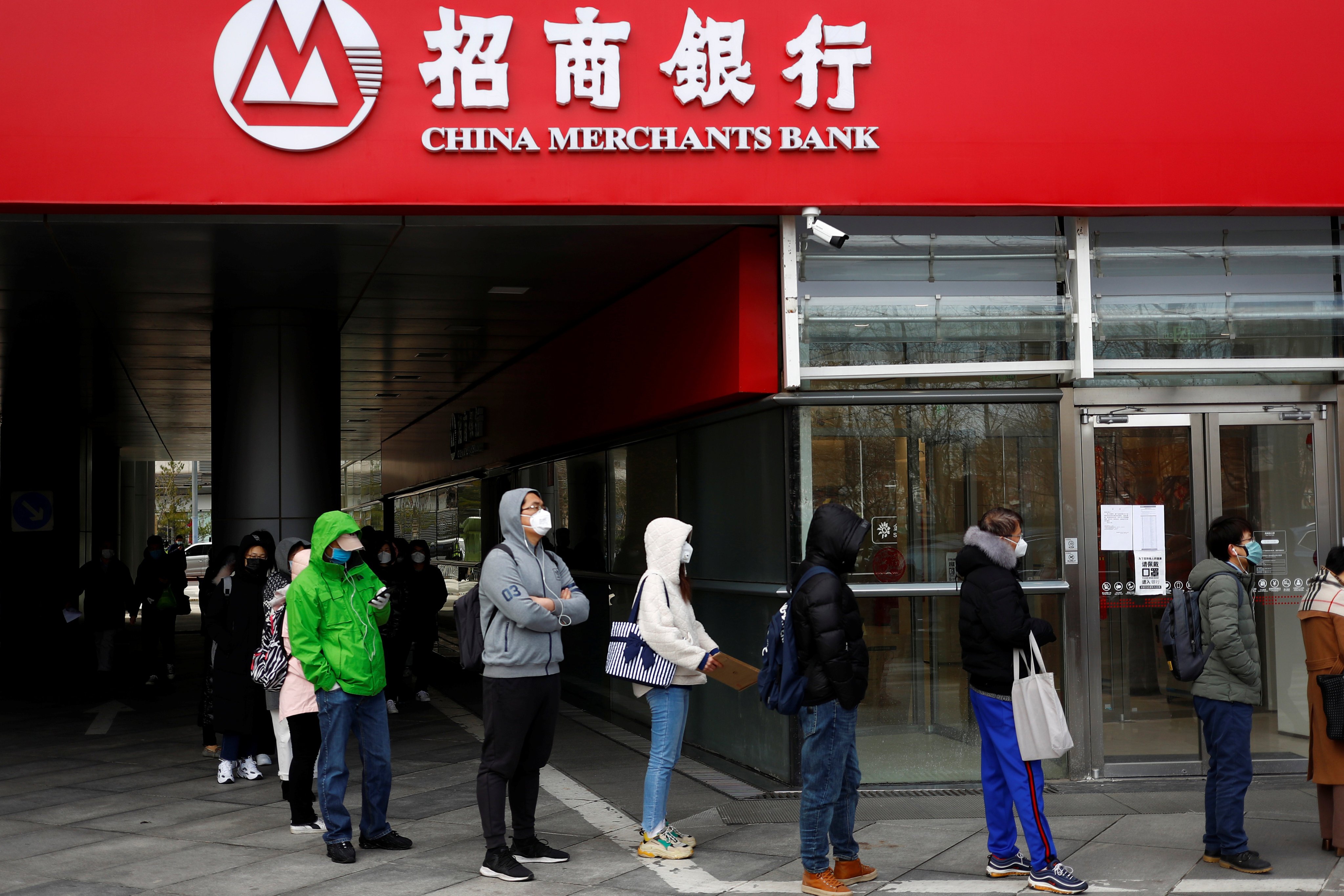 People wearing face masks line up near a branch of China Merchants Bank in Beijing in March 2020. Photo: Reuters
