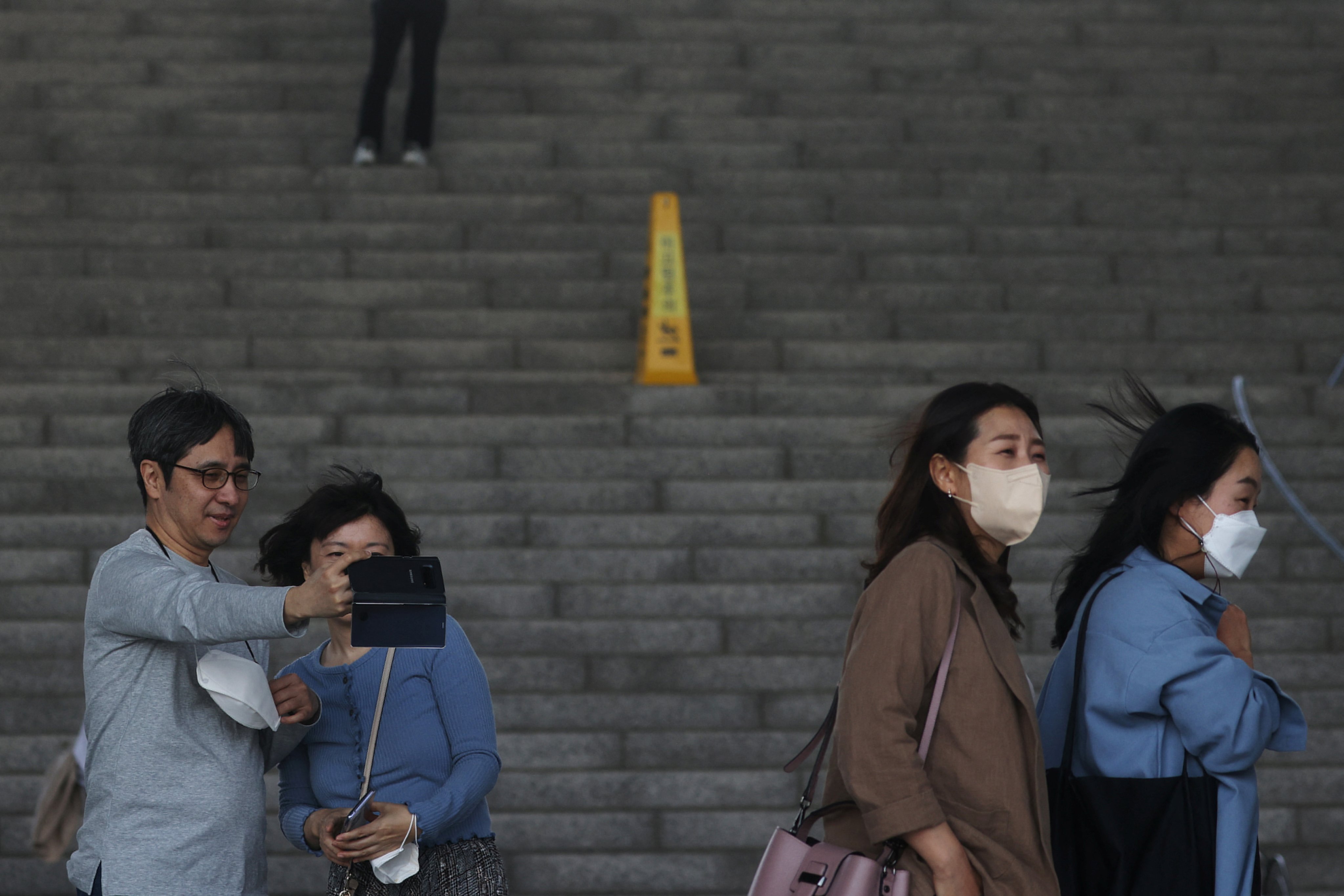 Women wearing protective masks to prevent contracting Covid-19 walk past a couple who takes a selfie photo without masks in Seoul, South Korea on Monday. Photo: Reuters