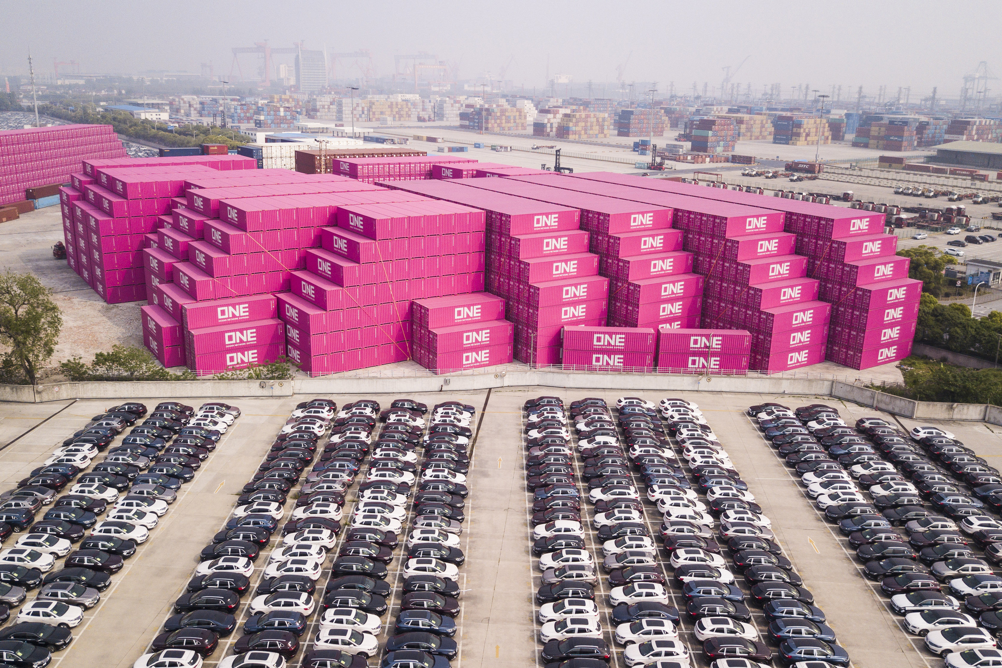 Vehicles awaiting exports next to stacks of containers by Ocean Network Express (ONE) in Shanghai on Monday, April 30, 2018. Photo: Bloomberg.