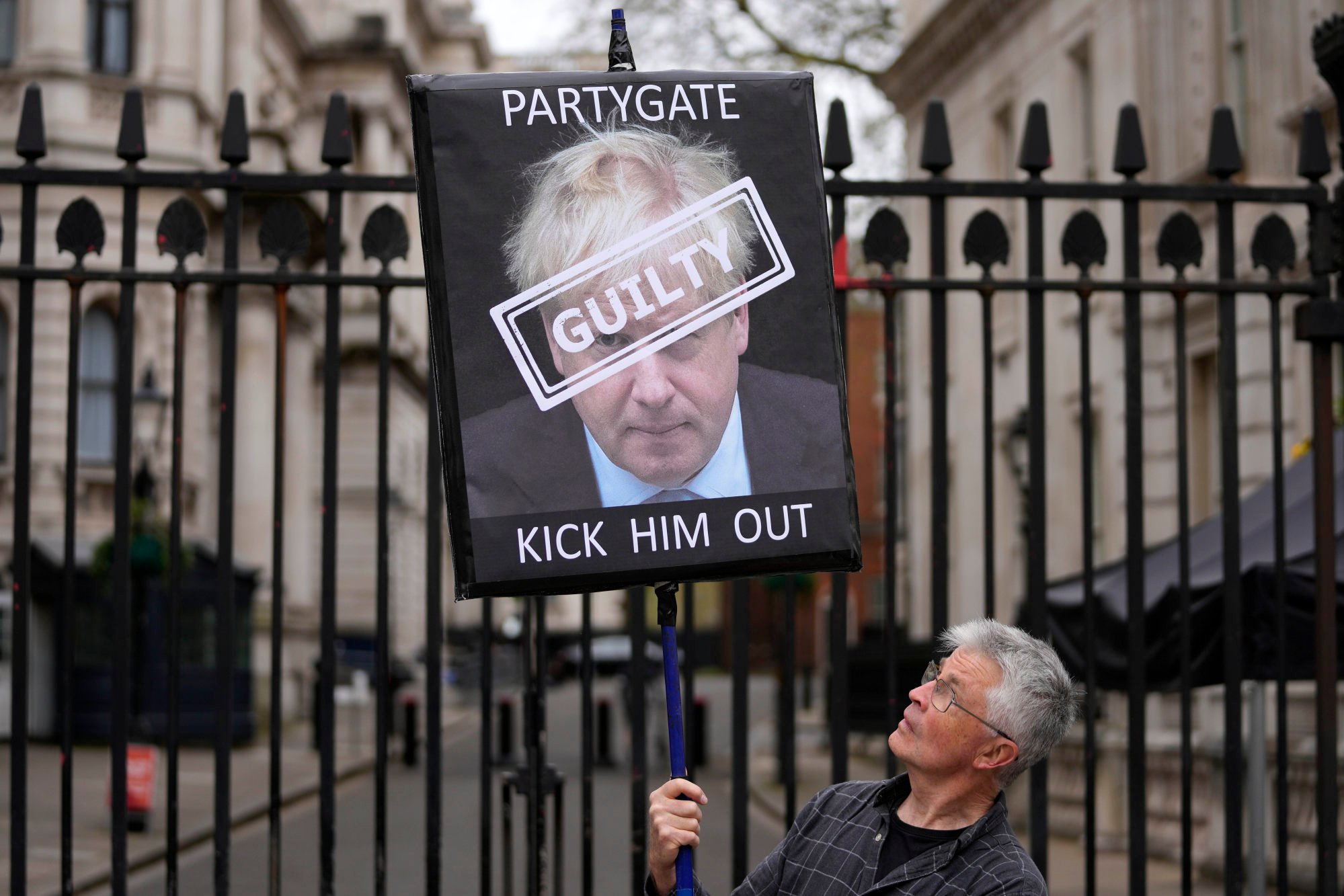 A protester holds a sign showing British Prime Minister Boris Johnson as he stands in front of the entrance to Downing Street in London in April. Photo: AP