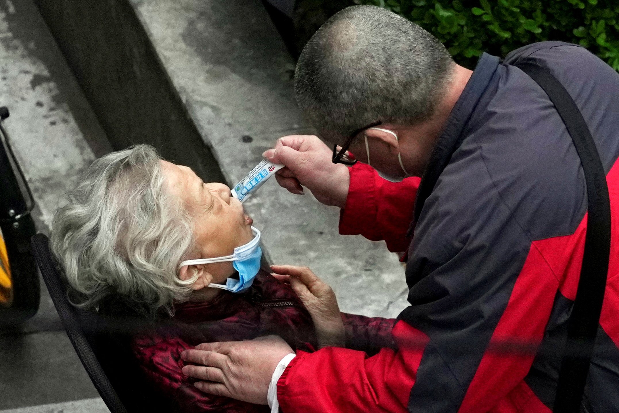 A man helps a woman consume a packet of Lianhua Qingwen as she sits by the side of a road outside a residential compound during a lockdown in Shanghai on April 5. Photo: Reuters