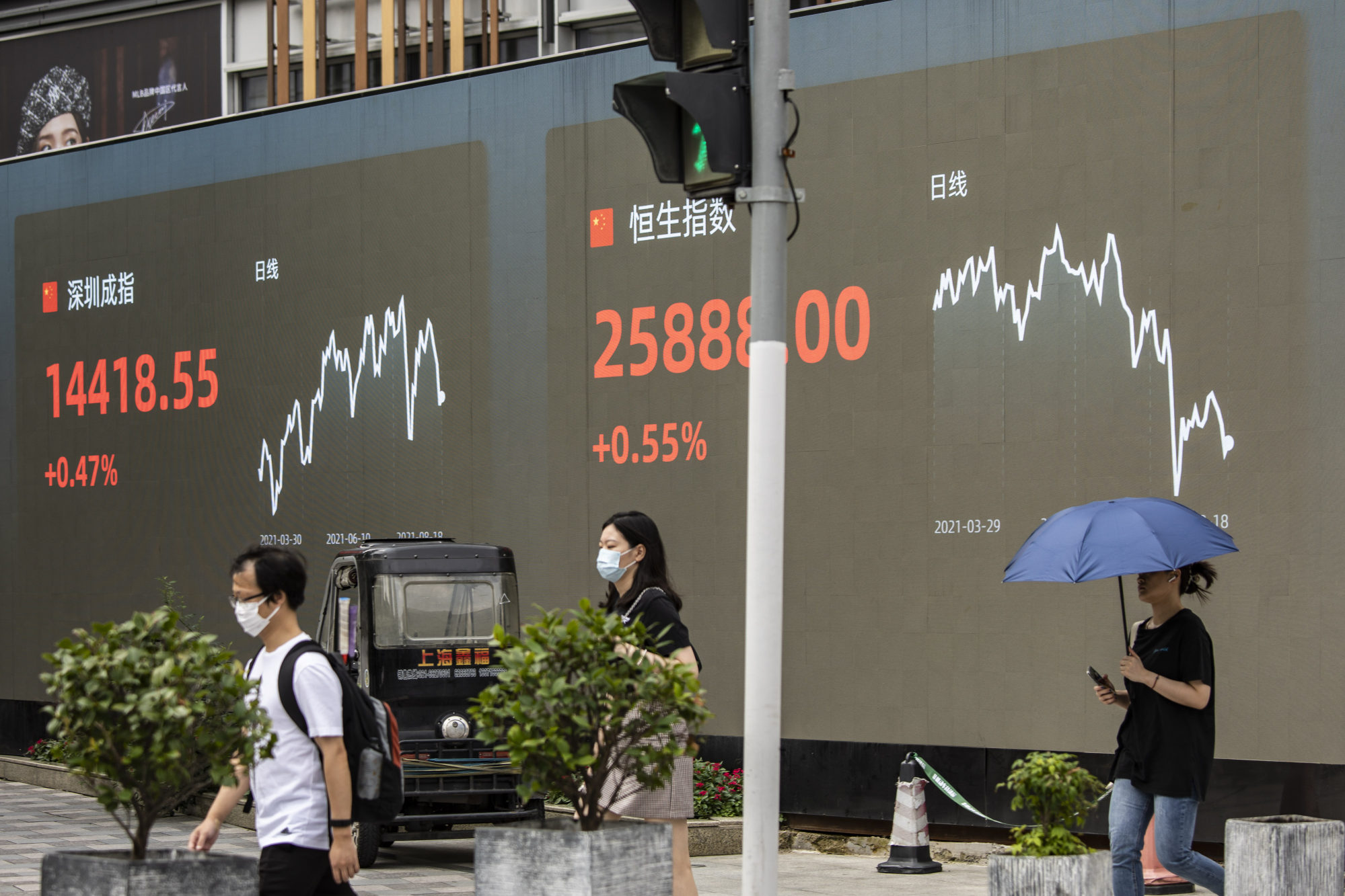 Pedestrians walk past a screen displaying the Shenzhen Stock Exchange and the Hang Seng Index figures in Shanghai. Photo: Bloomberg