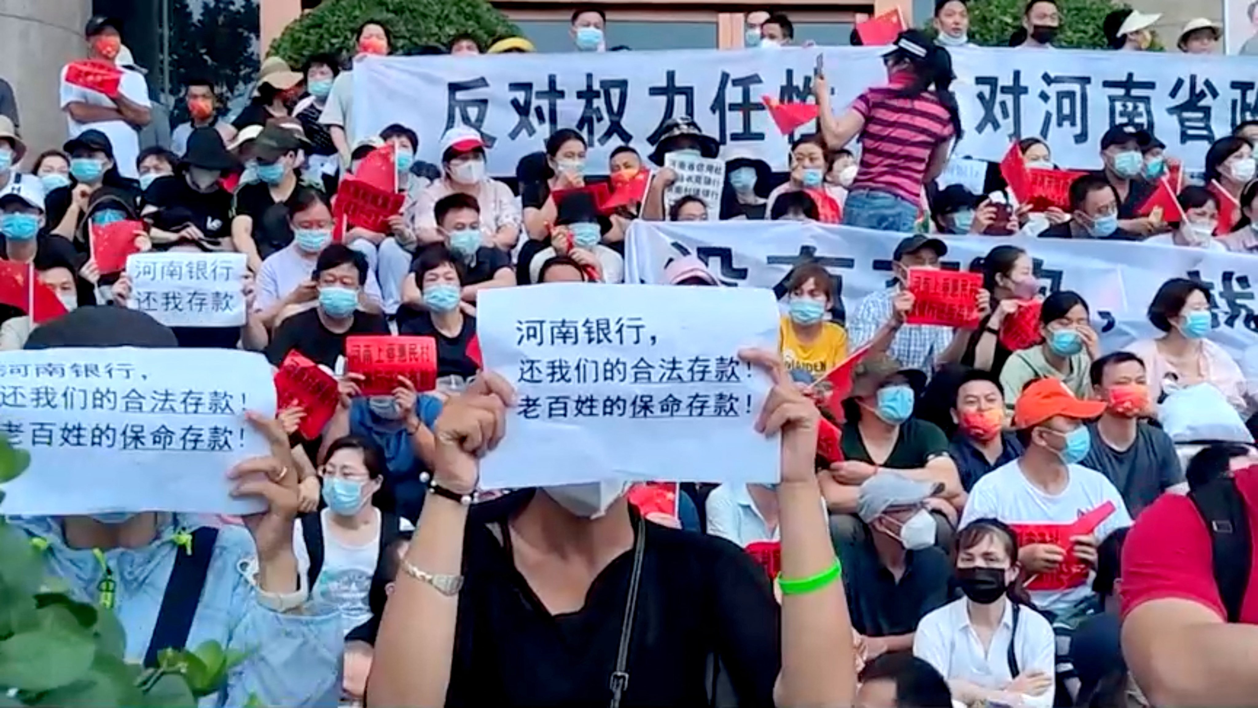 Demonstrators hold banners during a July 10 protest over the freezing of deposits by rural banks, outside a People’s Bank of China building in Zhengzhou, Henan province. Video screengrab via Reuters