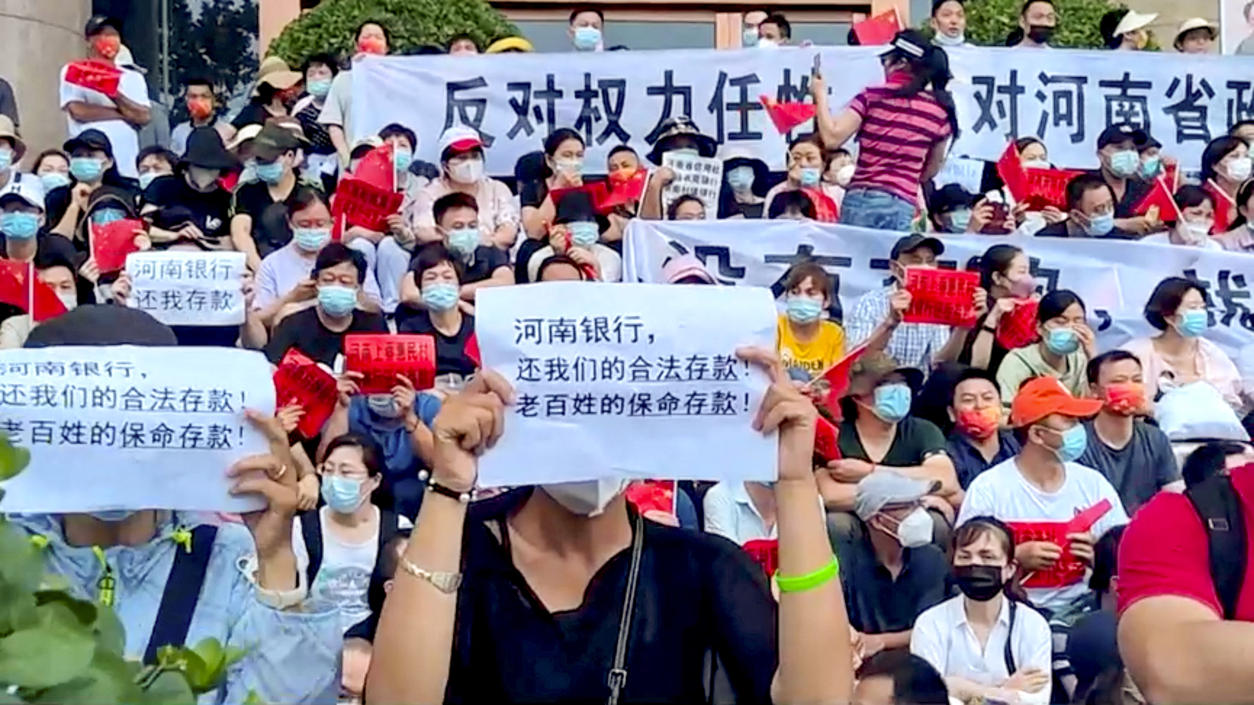 On Sunday, July 10, demonstrators hold up signs protesting against the freezing of deposits by some rural-based banks, outside a People’s Bank of China building in Zhengzhou, Henan province. The text in the foreground reads, “Henan Bank, return to us our legal deposits! The people’s life-saving deposits!” Photo: Reuters
