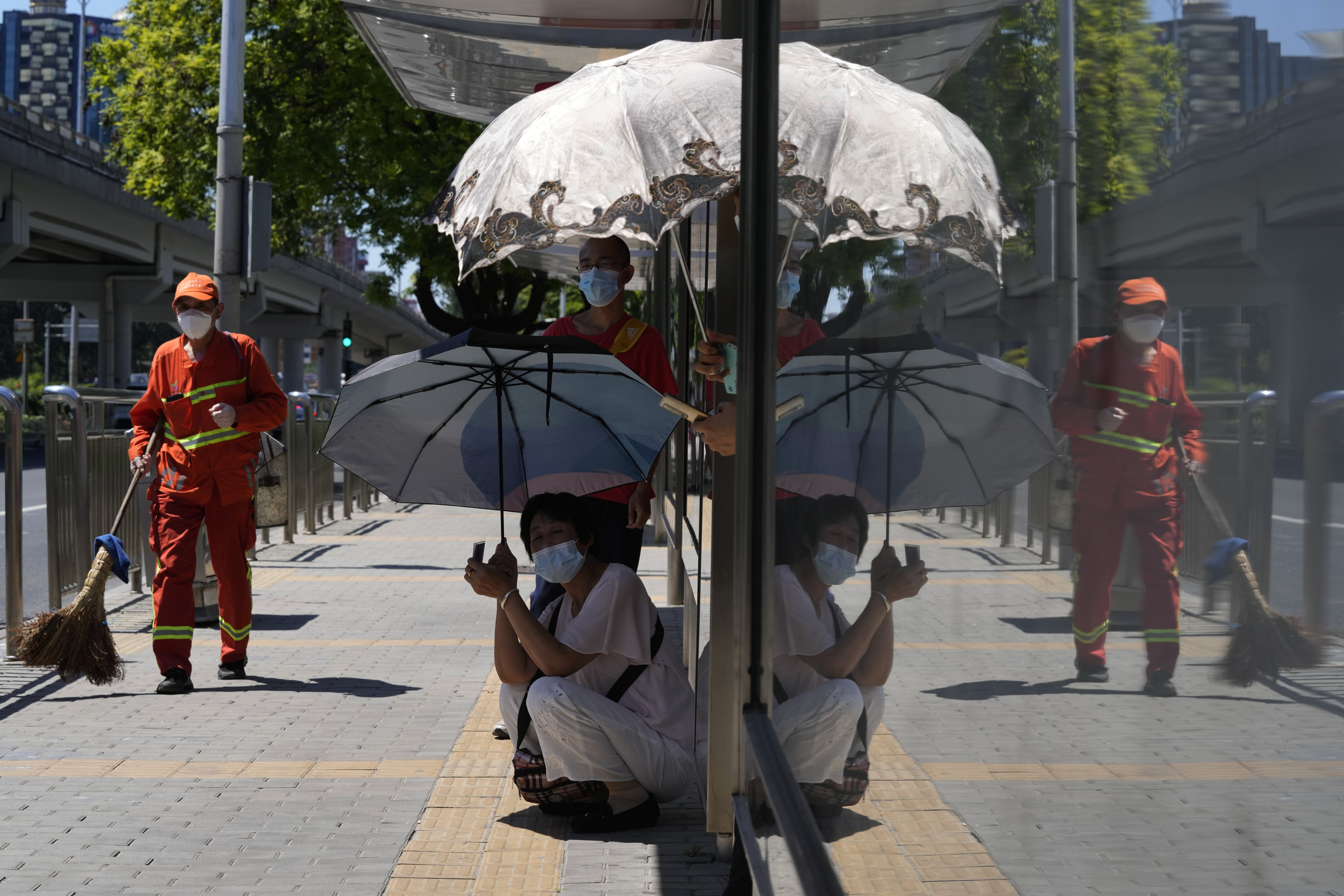 Residents take shelter from the sun as they wait for a bus in Beijing on July 15. Temperatures have surpassed all-time records as a heatwave sweeps across much of the country. Photo: AP