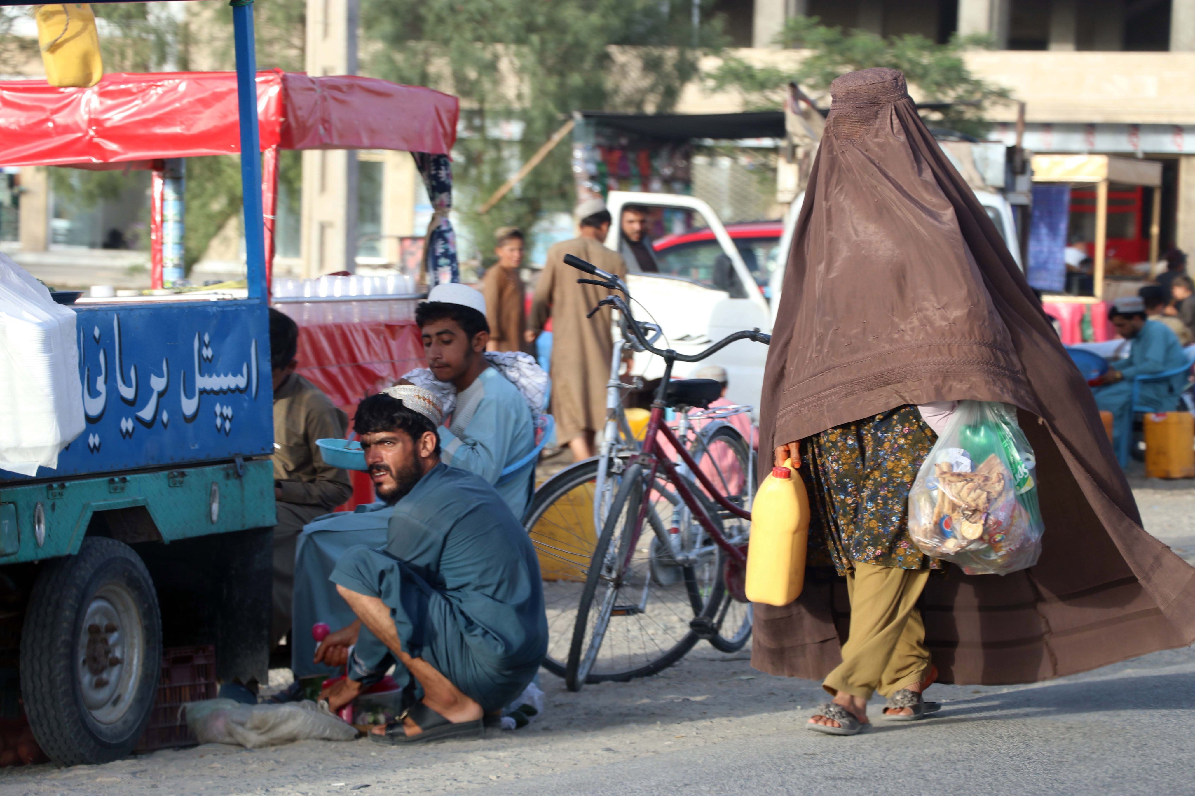 A burqa-clad Afghan woman walks past a roadside food vendor in Kandahar this month. Photo: EPA-EFE