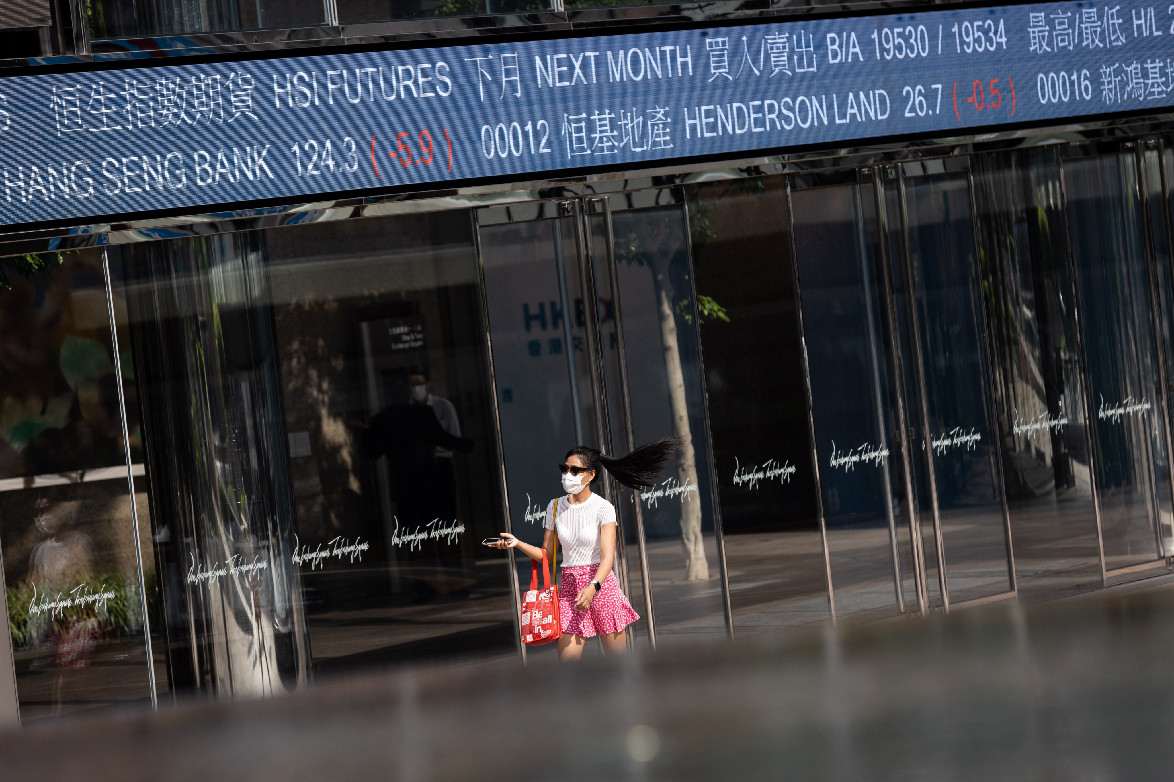 A woman walks past the Exchange Square in Central, Hong Kong with tickers showing stock prices. Photo: EPA-EFE