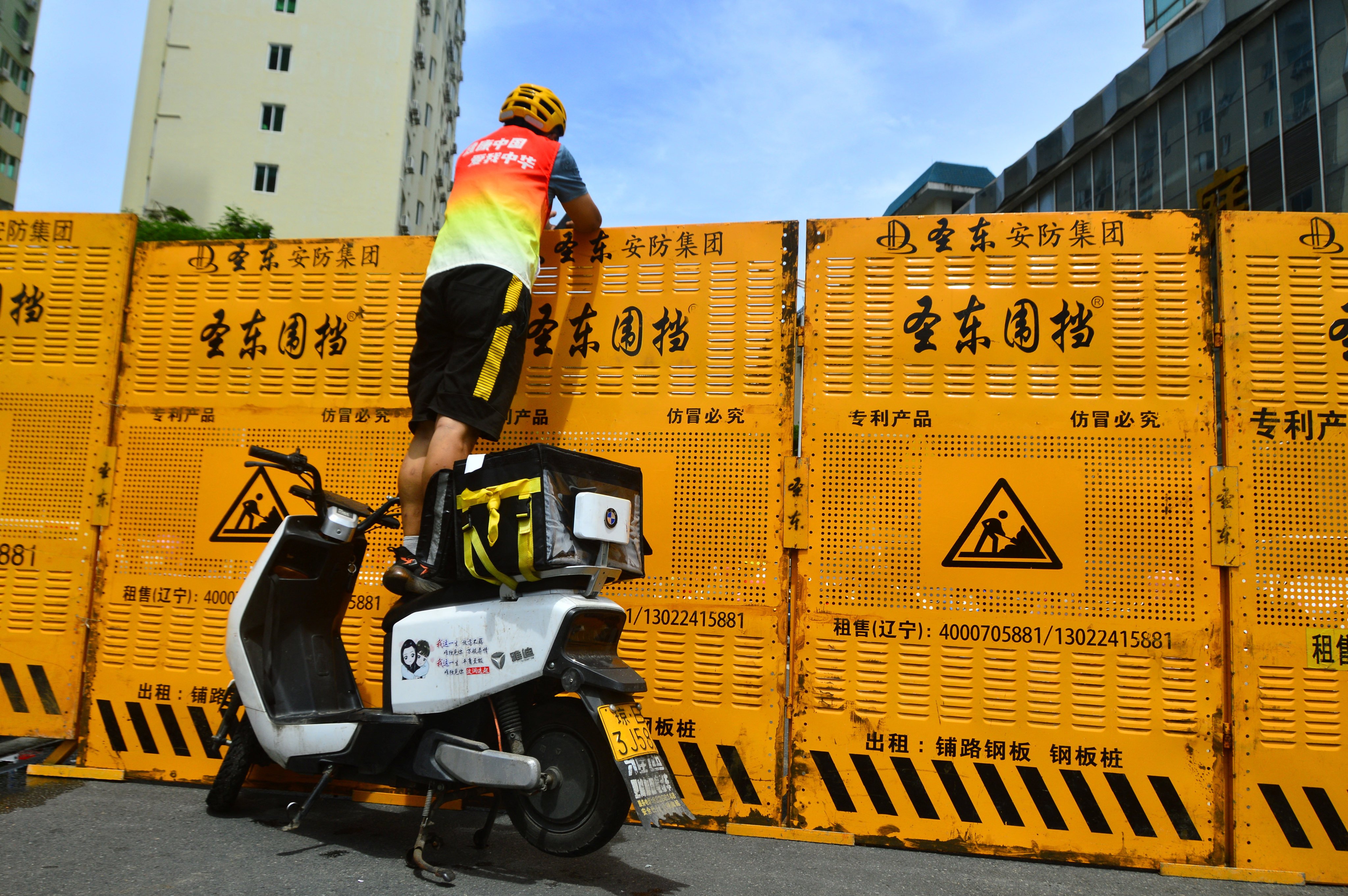 A courier makes a delivery over a barricade as Sanya goes into Covid-19 lockdown on August 6. Photo: via Reuters