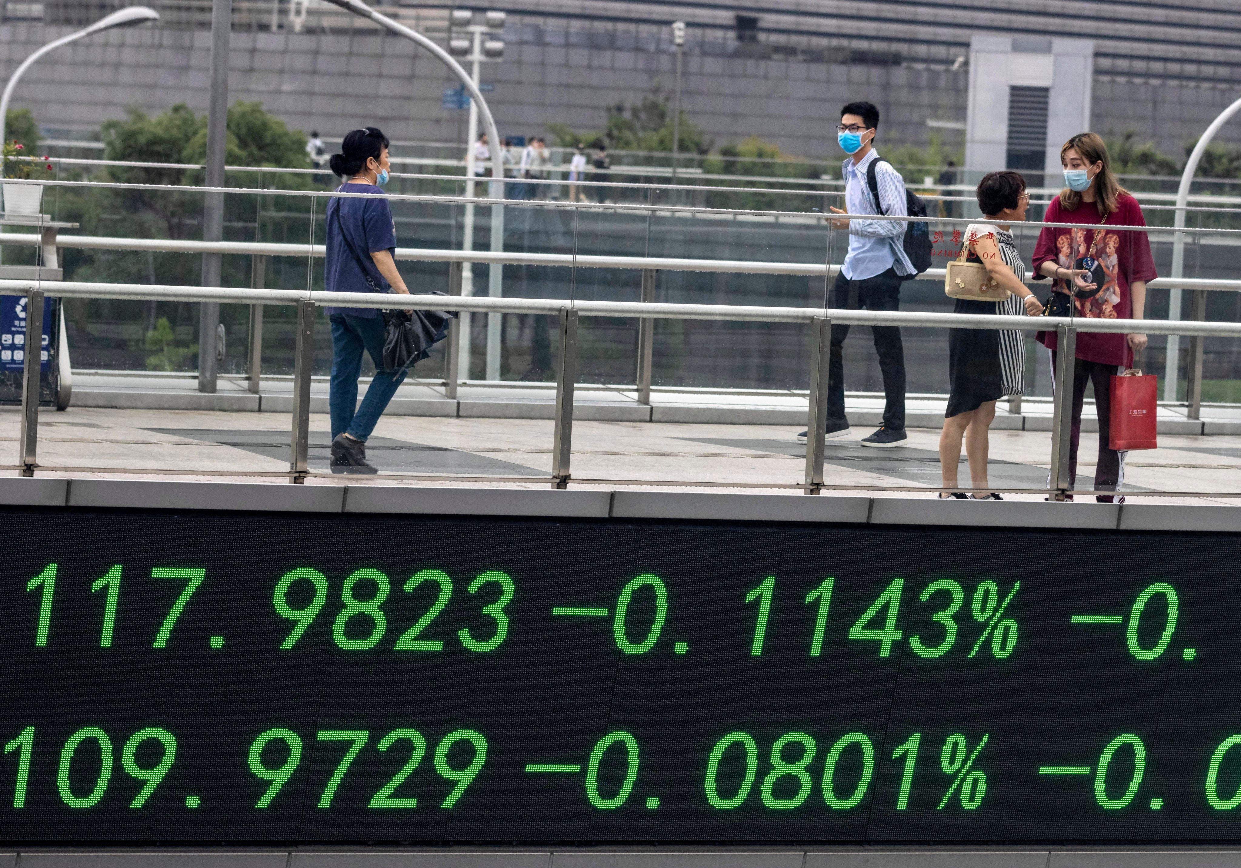 People walk over a pedestrian bridge that features a monitor for stock exchange values in Shanghai in July 2020. Photo: EPA-EFE