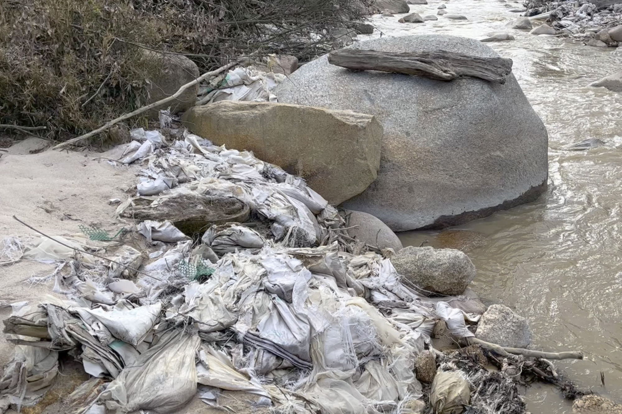 In this early 2022 image from a video provided by Global Witness, a creek in Myanmar’s Kachin State is lined with trash, pipes and other construction materials from a former rare earth mining site. Local villagers have said water from the creek is no longer usable for drinking. Exposure to contaminated water is one of the indicators that could be tracked. Photo: Global Witness via AP