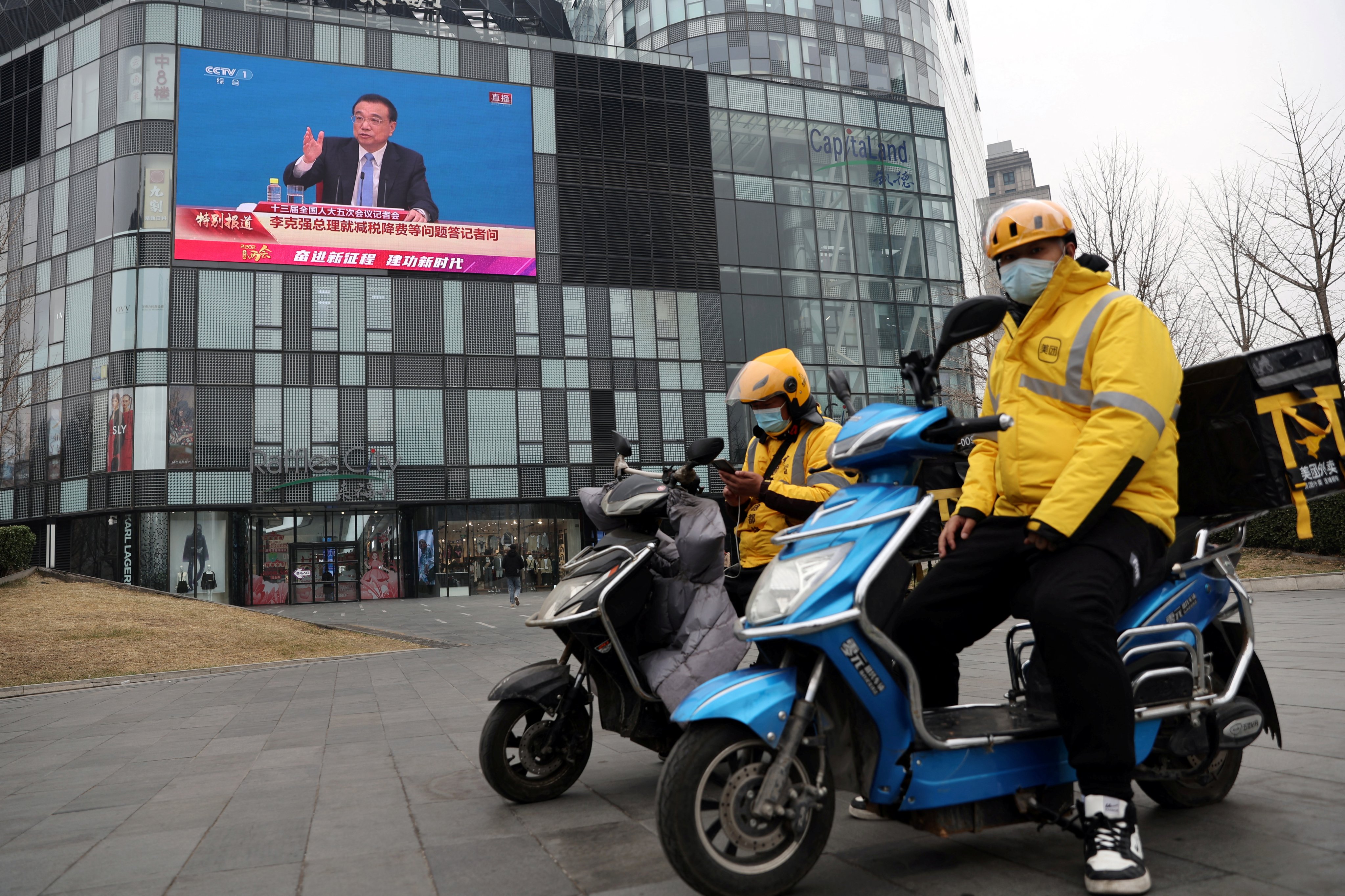 Meituan delivery drivers take a break near a giant screen showing a news conference by Premier Li Keqiang, following the closing session of the National People’s Congress in Beijing on March 11. Photo: Reuters 