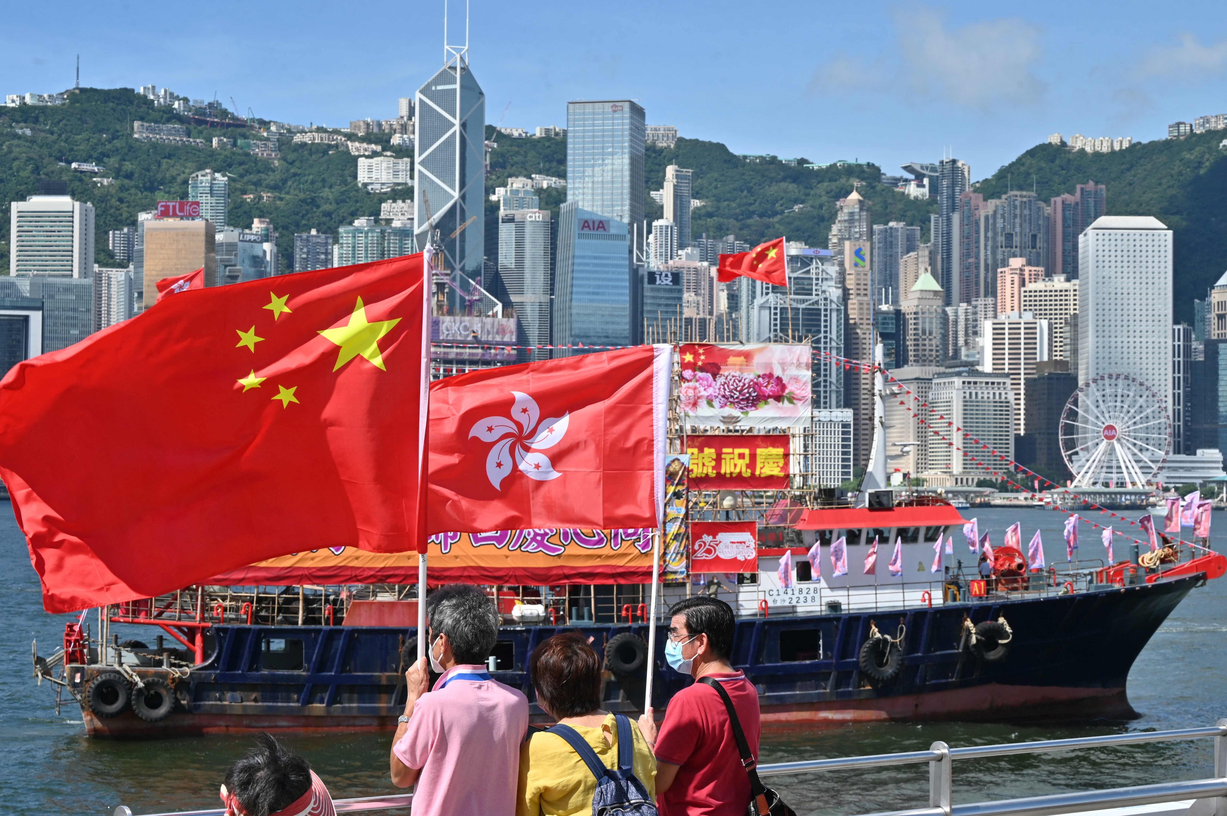 Onlookers wave national and Hong Kong flags as fishing boats marking the 25th anniversary of the handover sail through Victoria Harbour. Photo: AFP