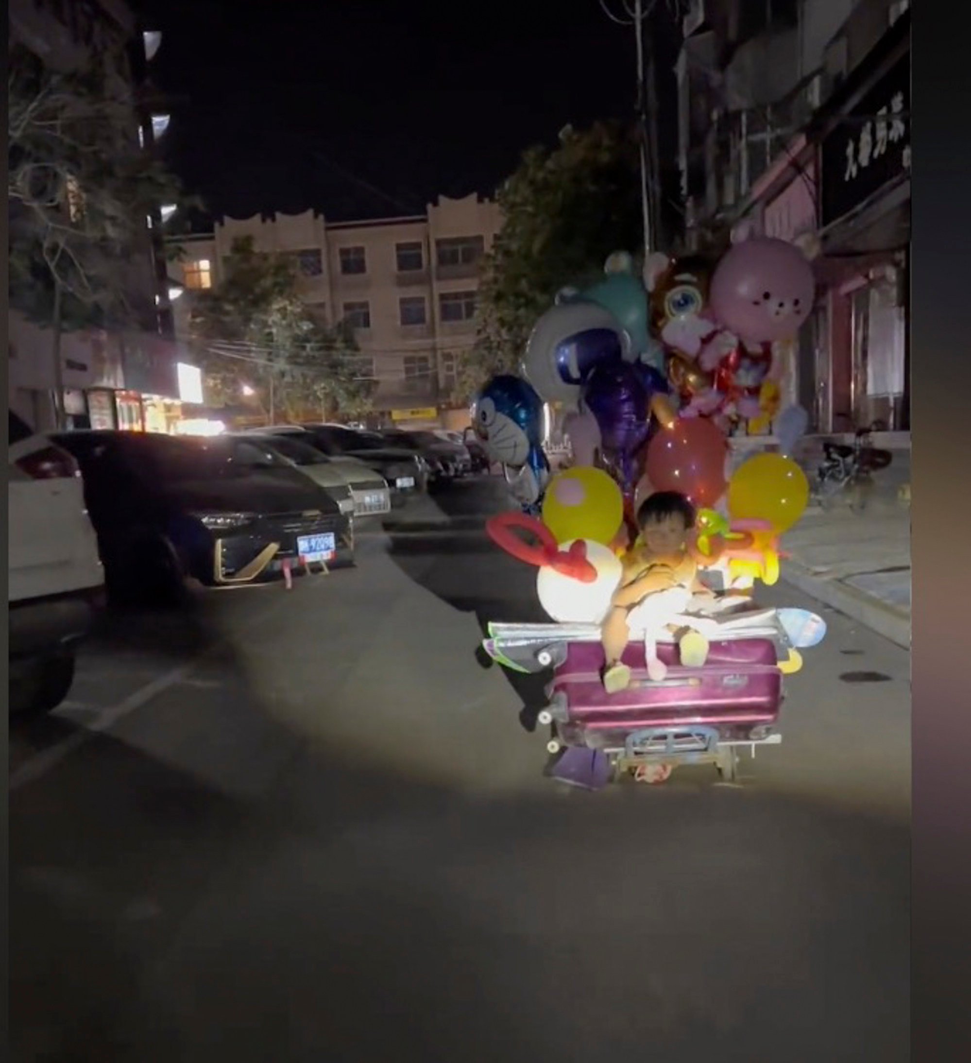 The unnamed little girl rides on top of her father’s luggage as he tries to sell balloons. Photo: Douyin