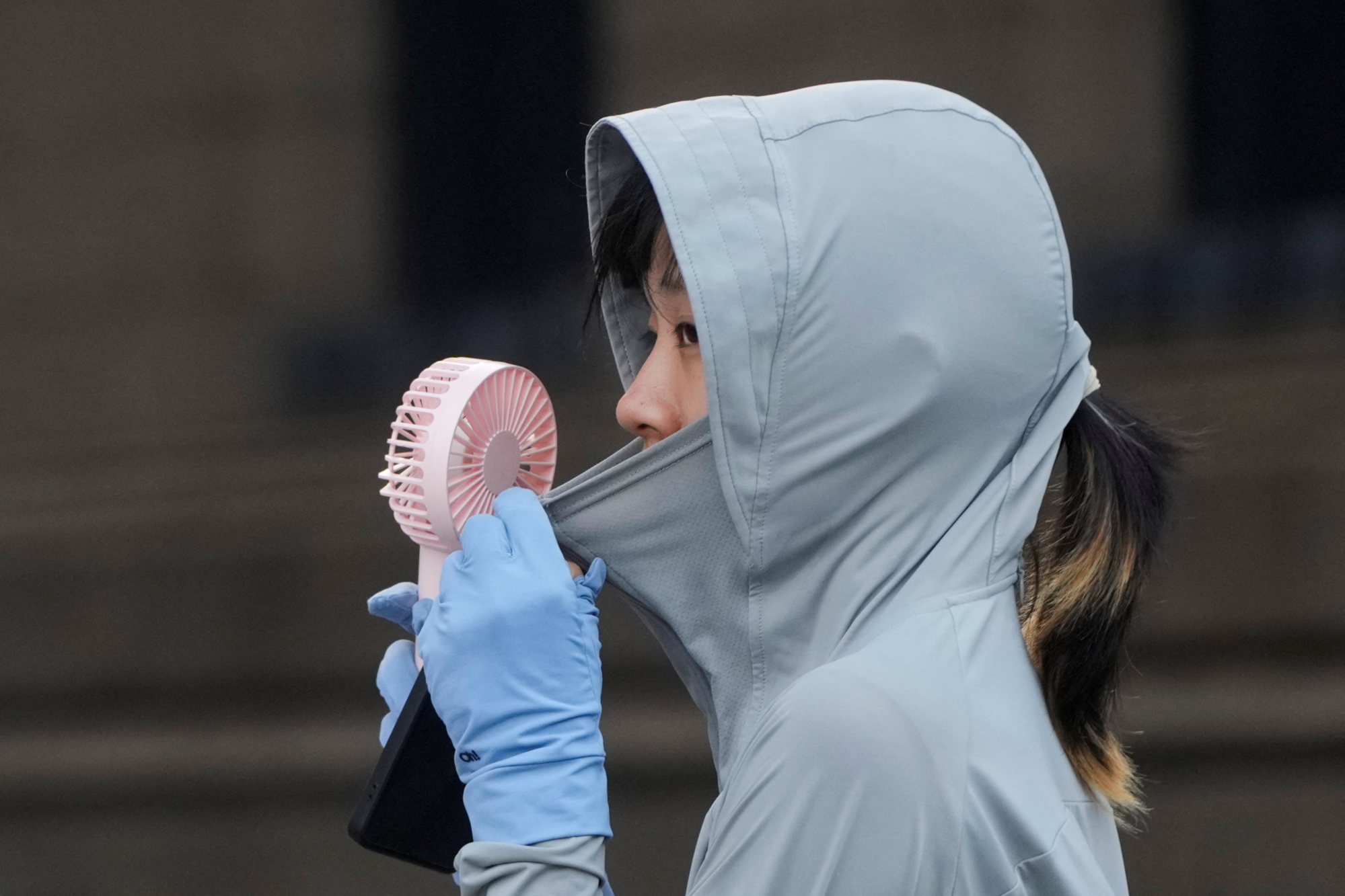 A woman uses a fan as she wears a cloth that protects her from the sun on a street, amid a heatwave warning in Shanghai. Photo: Reuters