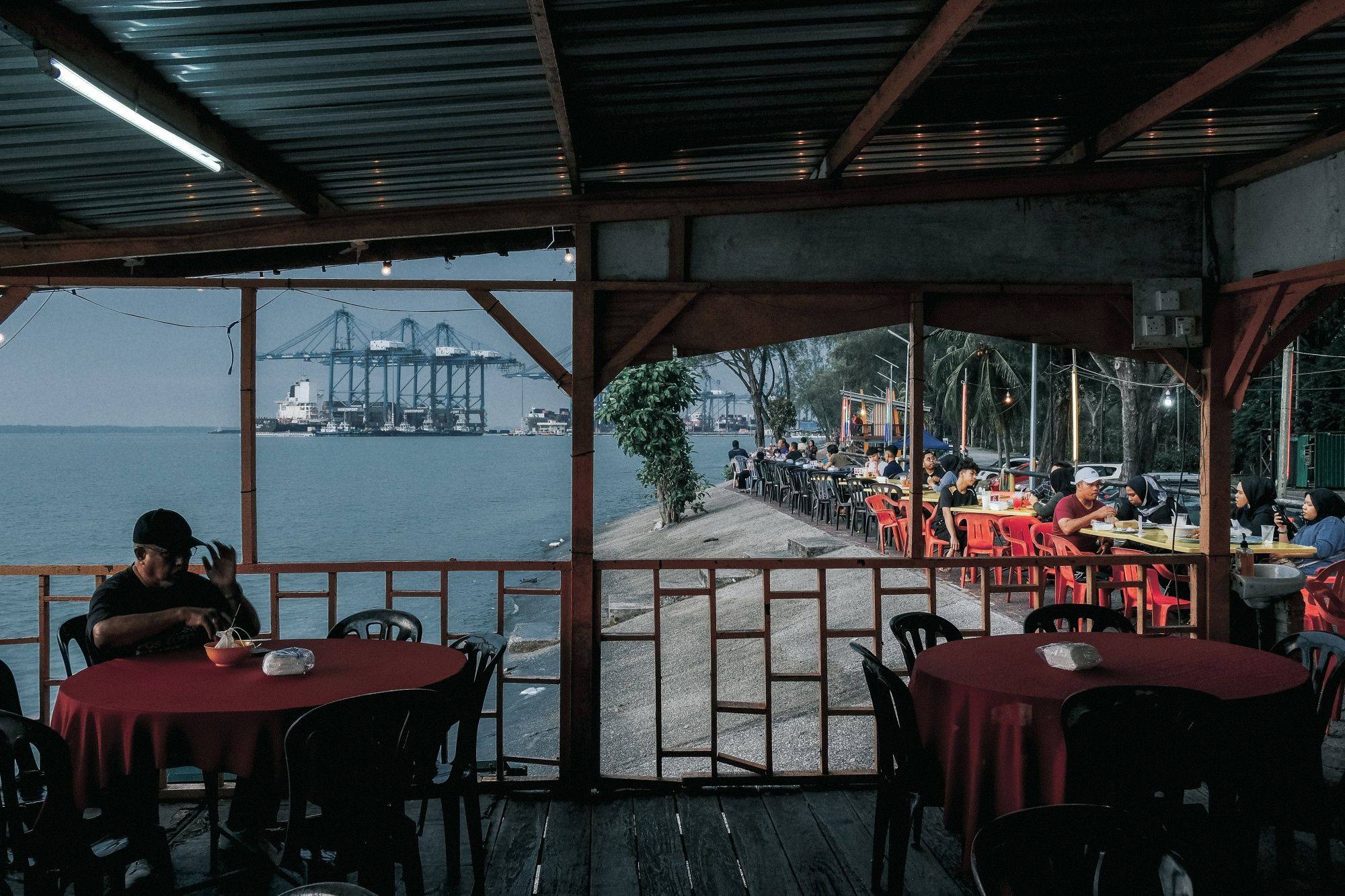 Customers sit in a restaurant with gantry cranes in the background at Port Klang, Selangor, Malaysia, on August 12. As countries reopen, intraregional trade in Asia could help offset the effects of economic slowdowns elsewhere. Photo: Bloomberg