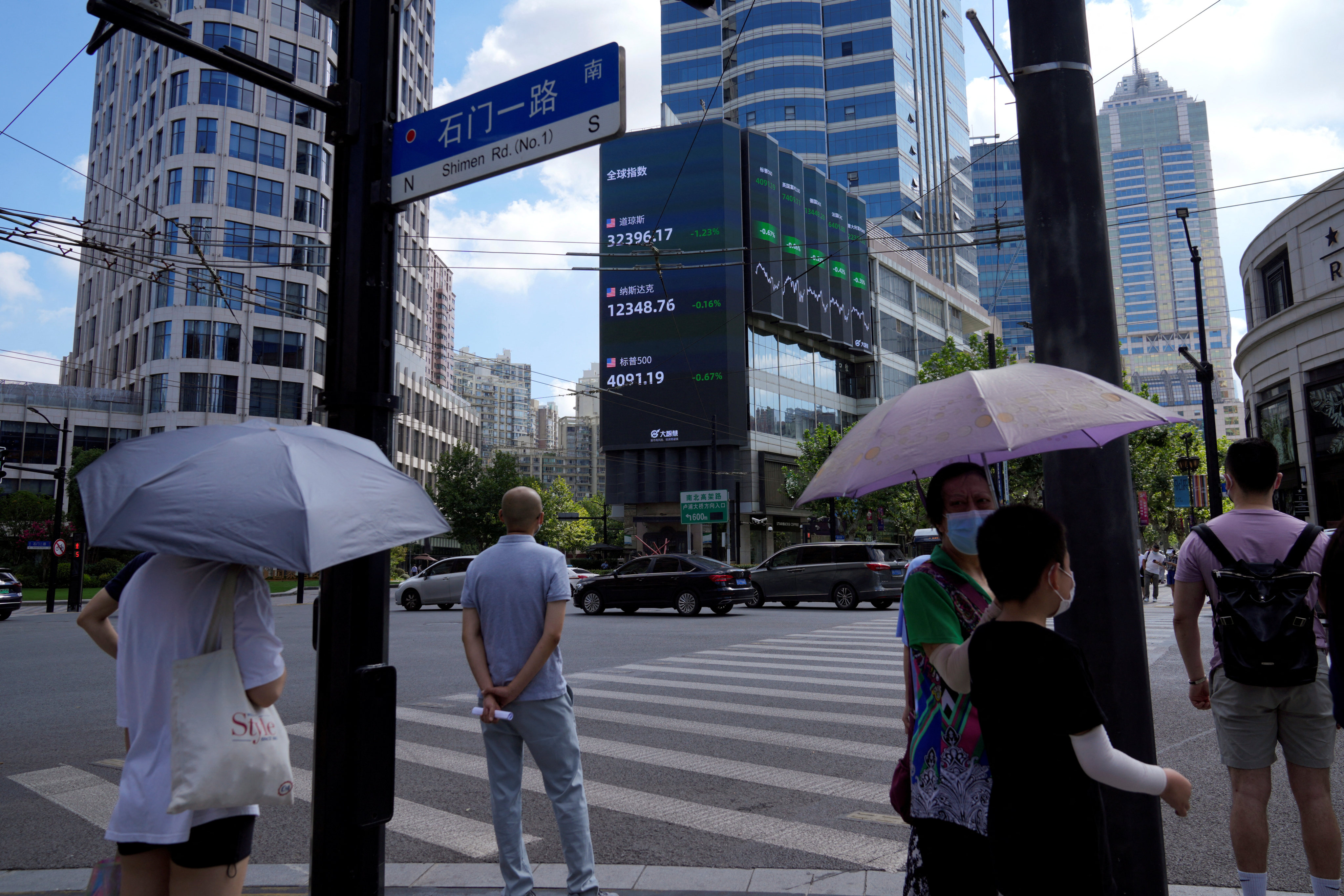 Pedestrians wait to cross a road at a junction near a giant display of stock indexes in Shanghai on August 3. Reuters