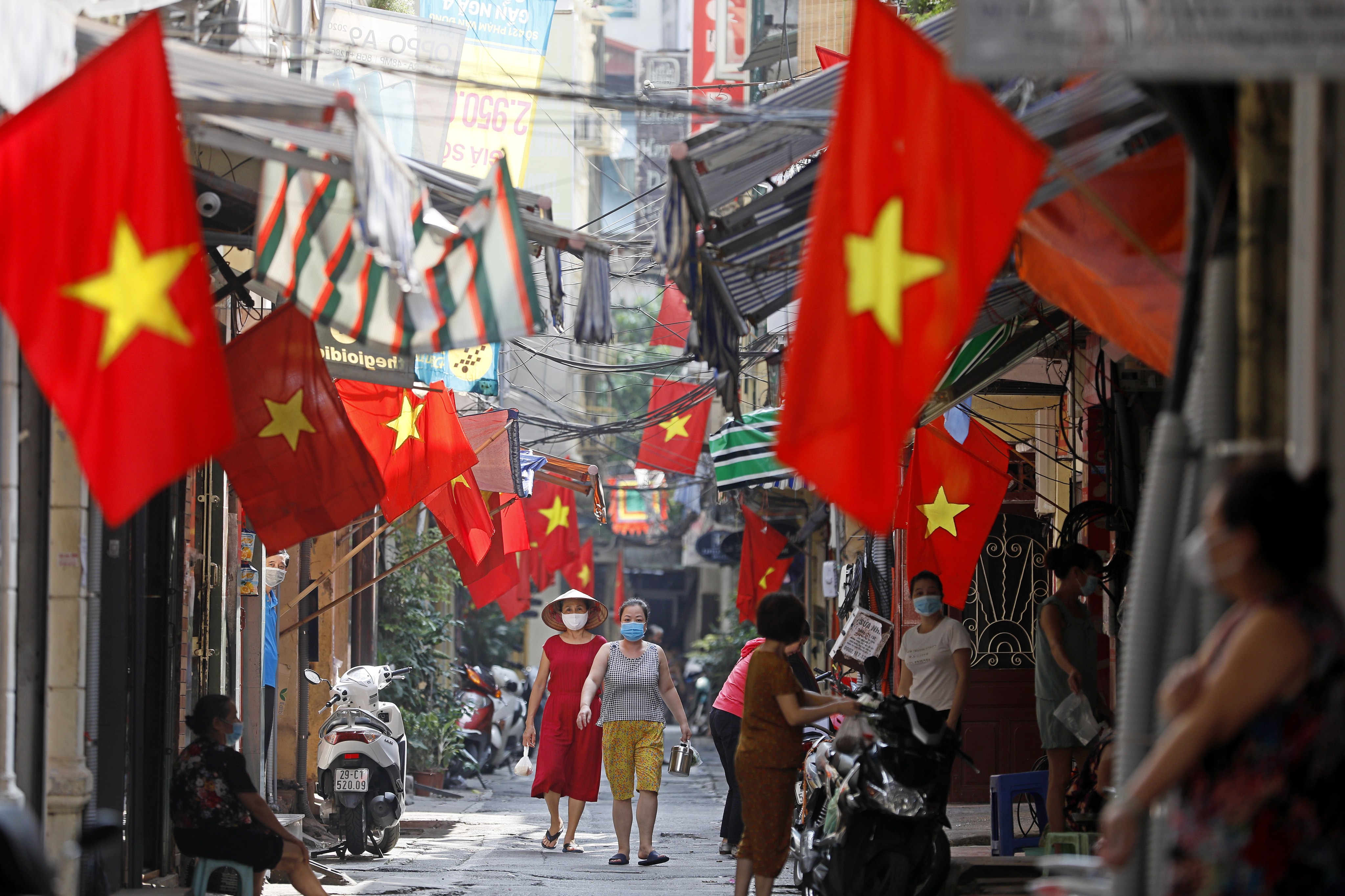 People walk under Vietnamese national flags at an alley in Hanoi. Photo: EPA-EFE