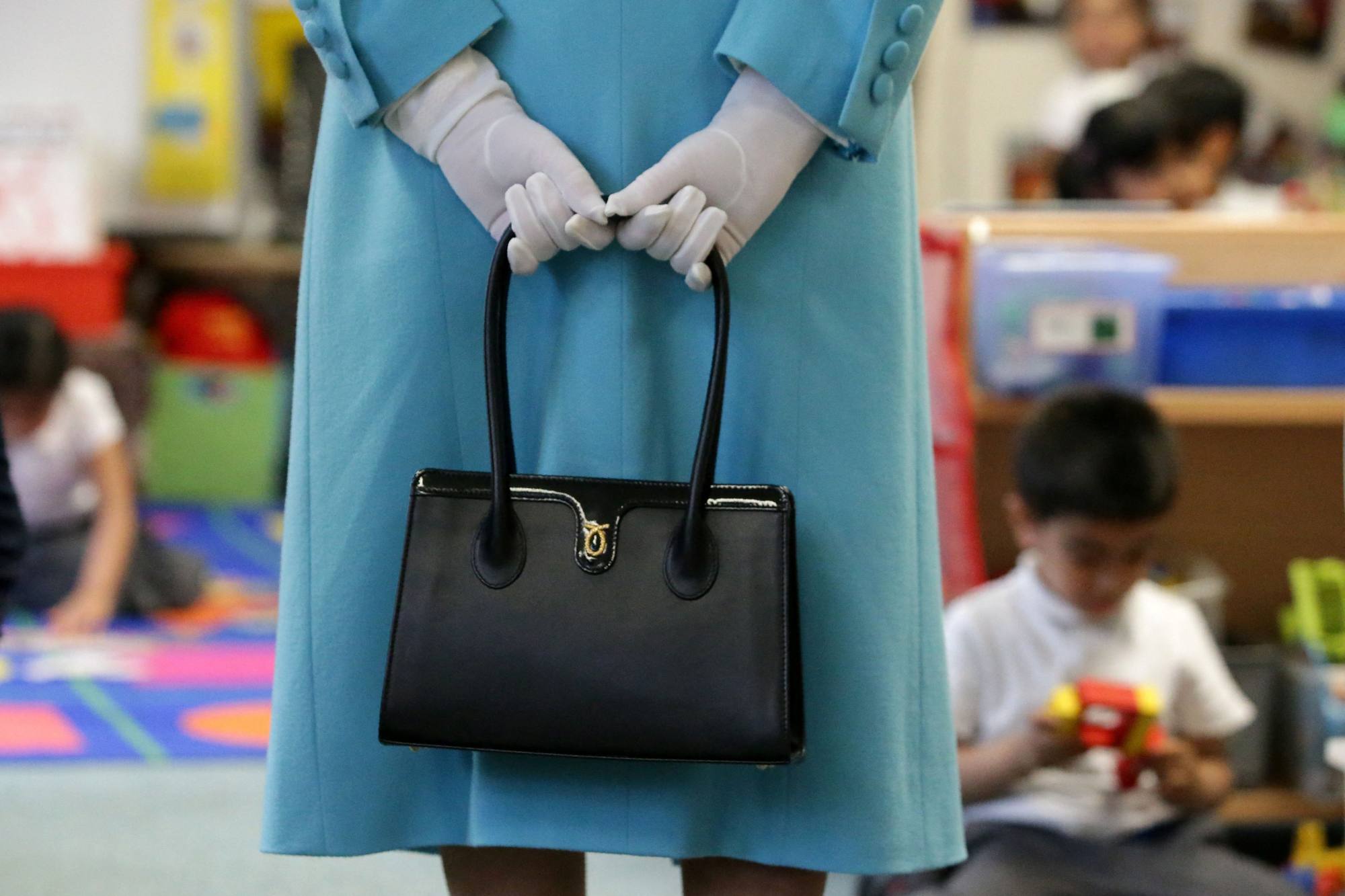 Queen Elizabeth keeps hold of her Launer handbags as she tours a school in London in 2017. Photo: AFP/Pool