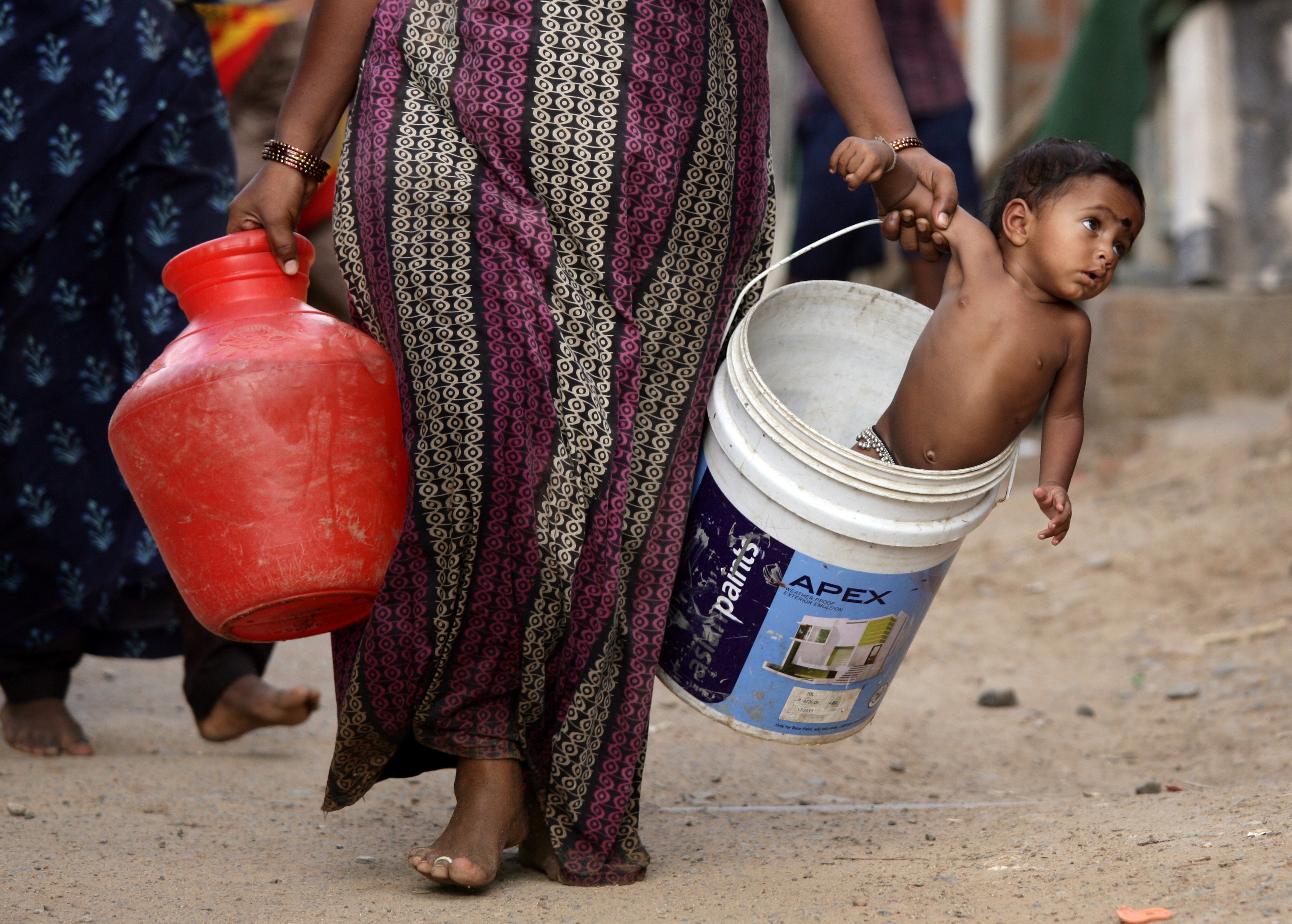 A woman carries her son in a bucket after collecting water from a municipal tanker on the outskirts of Chennai, India, on July 4, 2019. Photo: Reuters