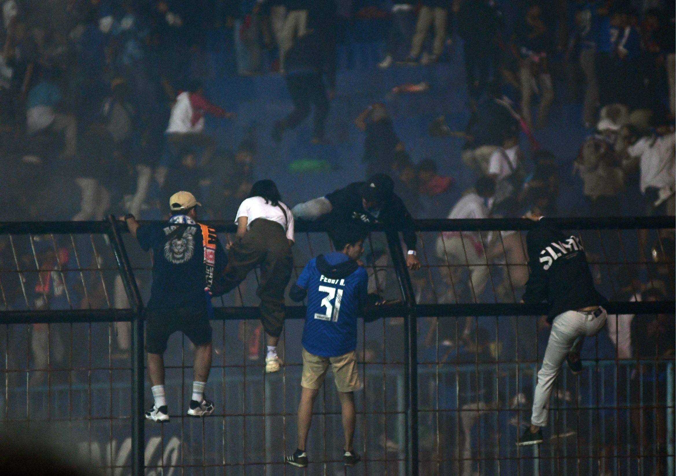 Spectators climb a fence by the stands amid a deadly stampede after a football match in Indonesia. Photo: AFP/File