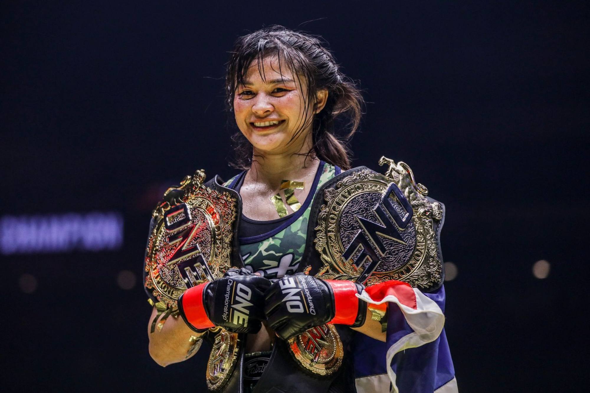 Stamp Fairtex holding the ONE atomweight Muay Thai and kickboxing belts.