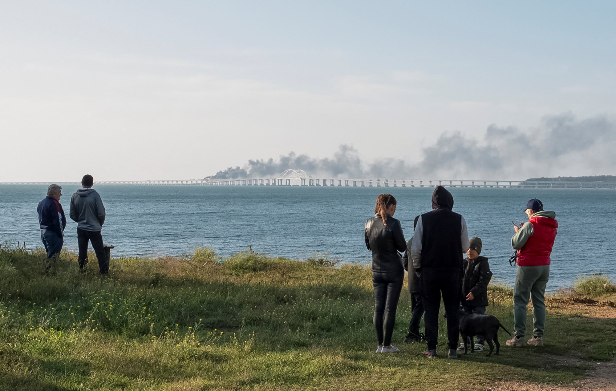 People watch fuel tanks ablaze and damaged sections of the Kerch bridge in the Kerch Strait, Crimea. Photo: Reuters