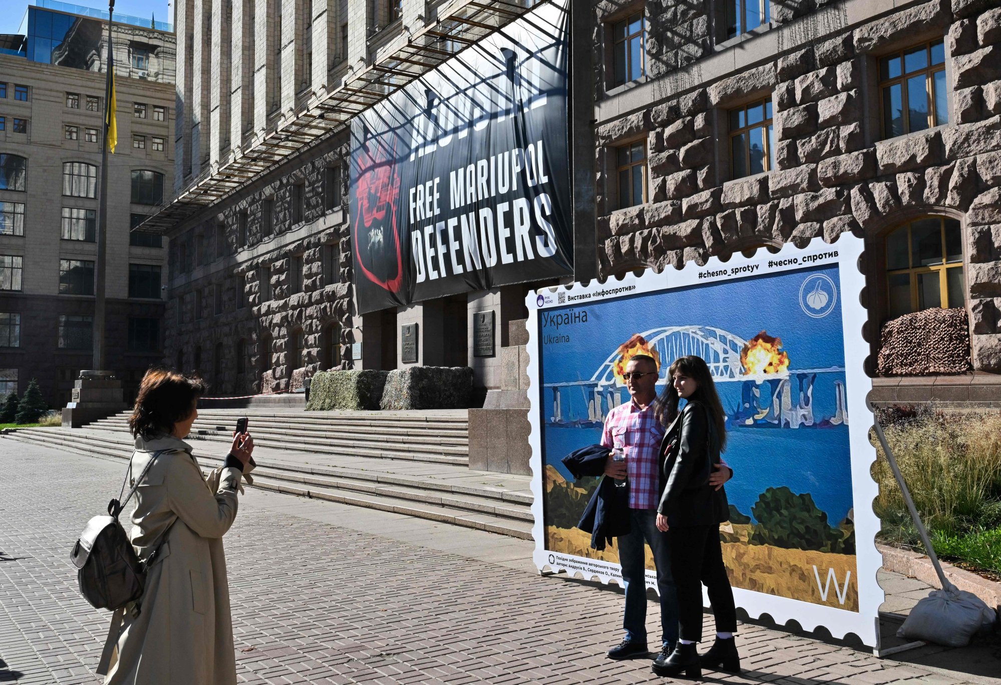 A couple poses in front of an artwork shaped as a big stamp entitled (with a play on words) “Cotton to the Crimean Bridge” depicting the October 8 explosion on Kerch bridge, set in the centre of Ukrainian capital of Kyiv. Photo: AFP