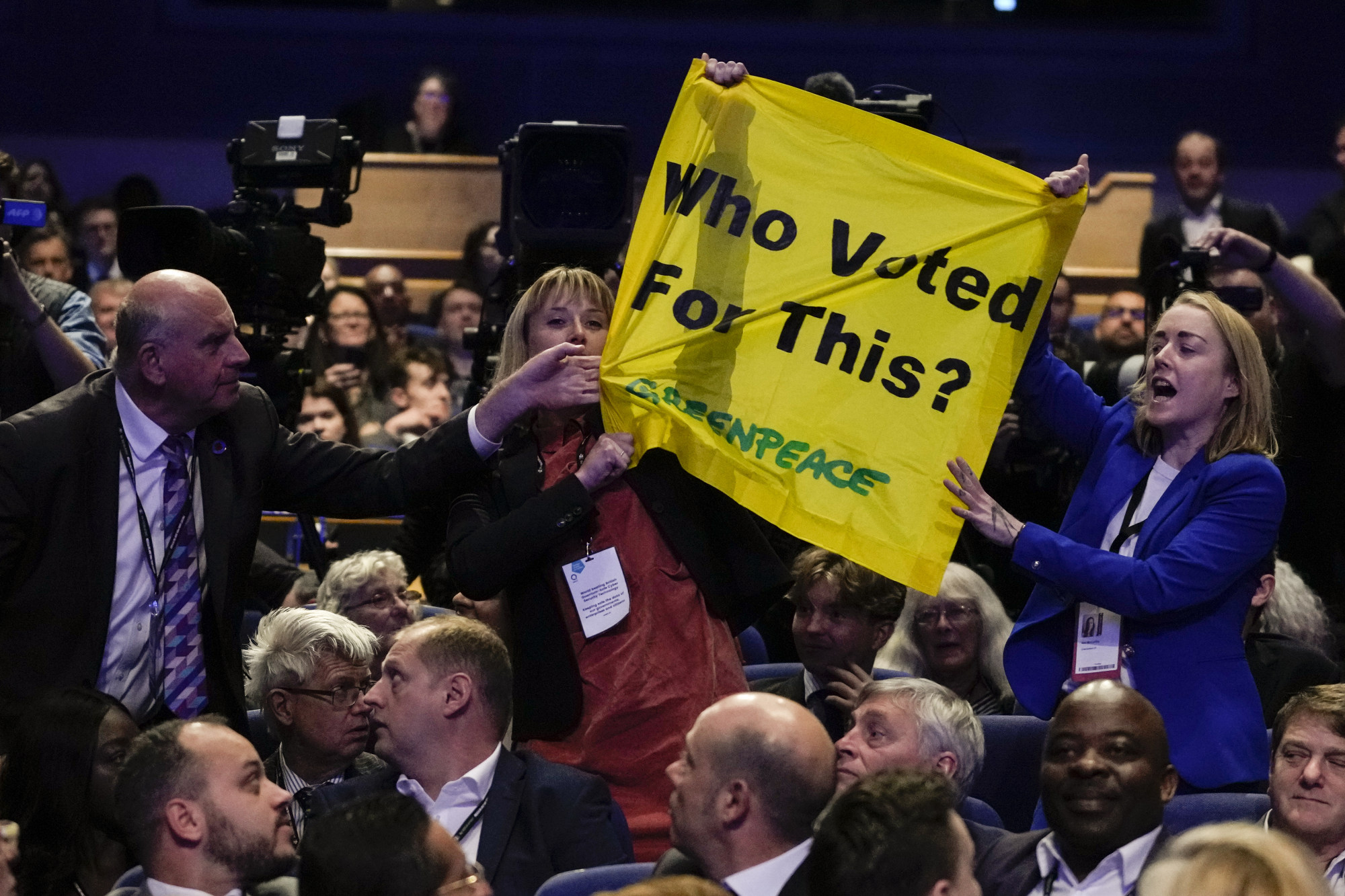 A man pulls down a banner held by two protesters as Britain’s Prime Minister Liz Truss makes a speech at the Conservative Party conference in Birmingham, England earlier this month. Photo: AP