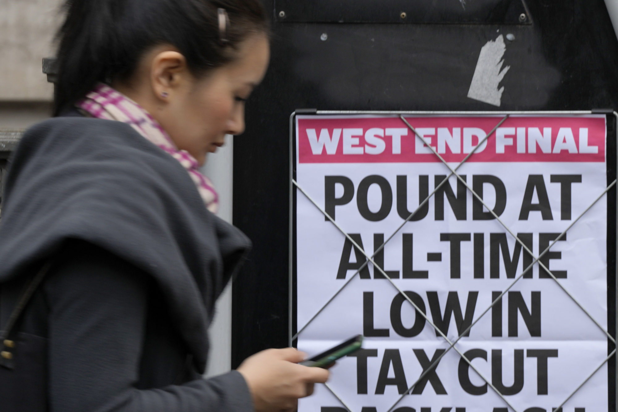 A woman walks past a headline posted on a wall in London in September 2022 after the British pound plunged to a record low against the US dollar. Photo: AP