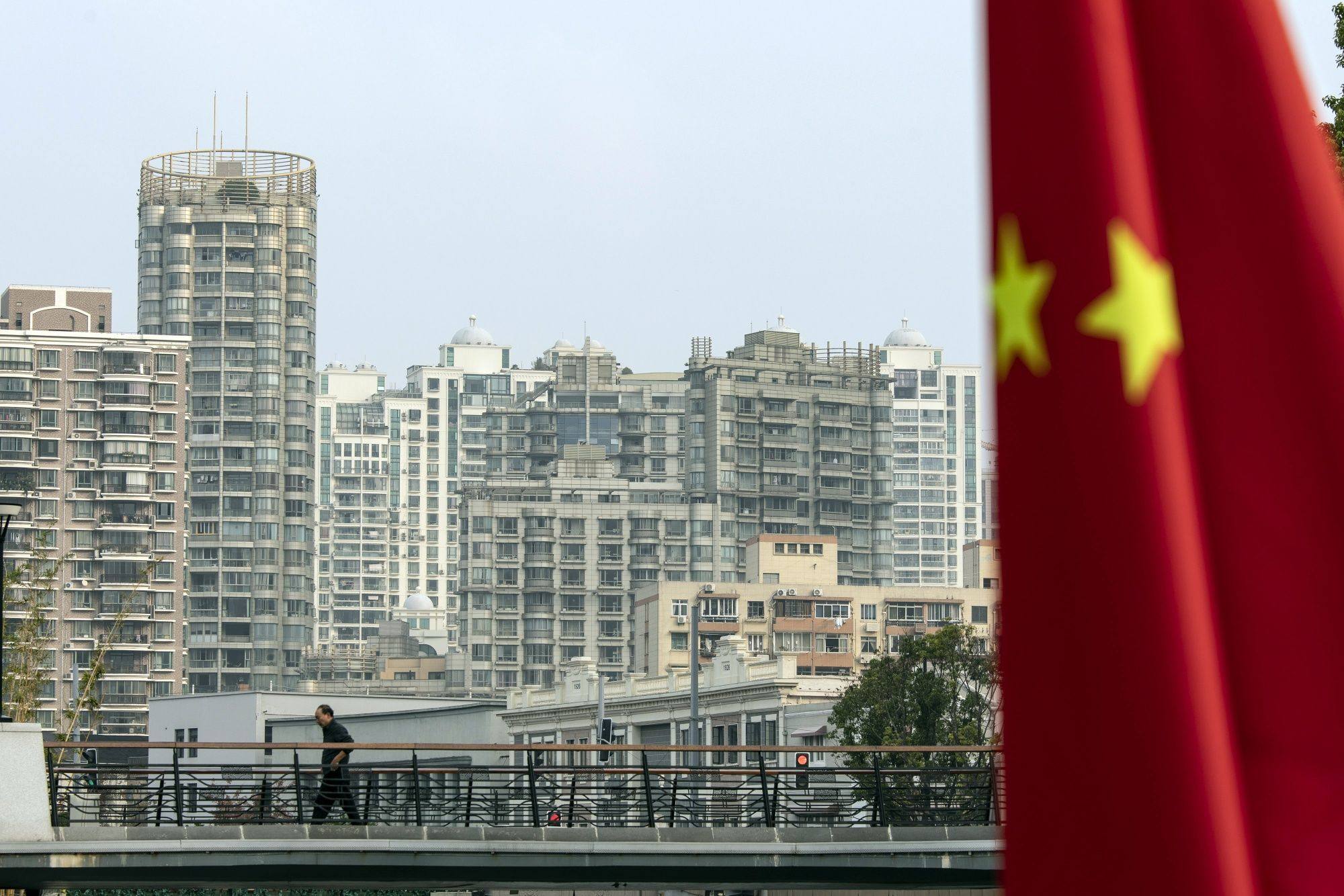 A Chinese flag in front of residential buildings in Shanghai. Sluggish demand and sentiment is hurting new home sales and prices across the country. Photo: Bloomberg