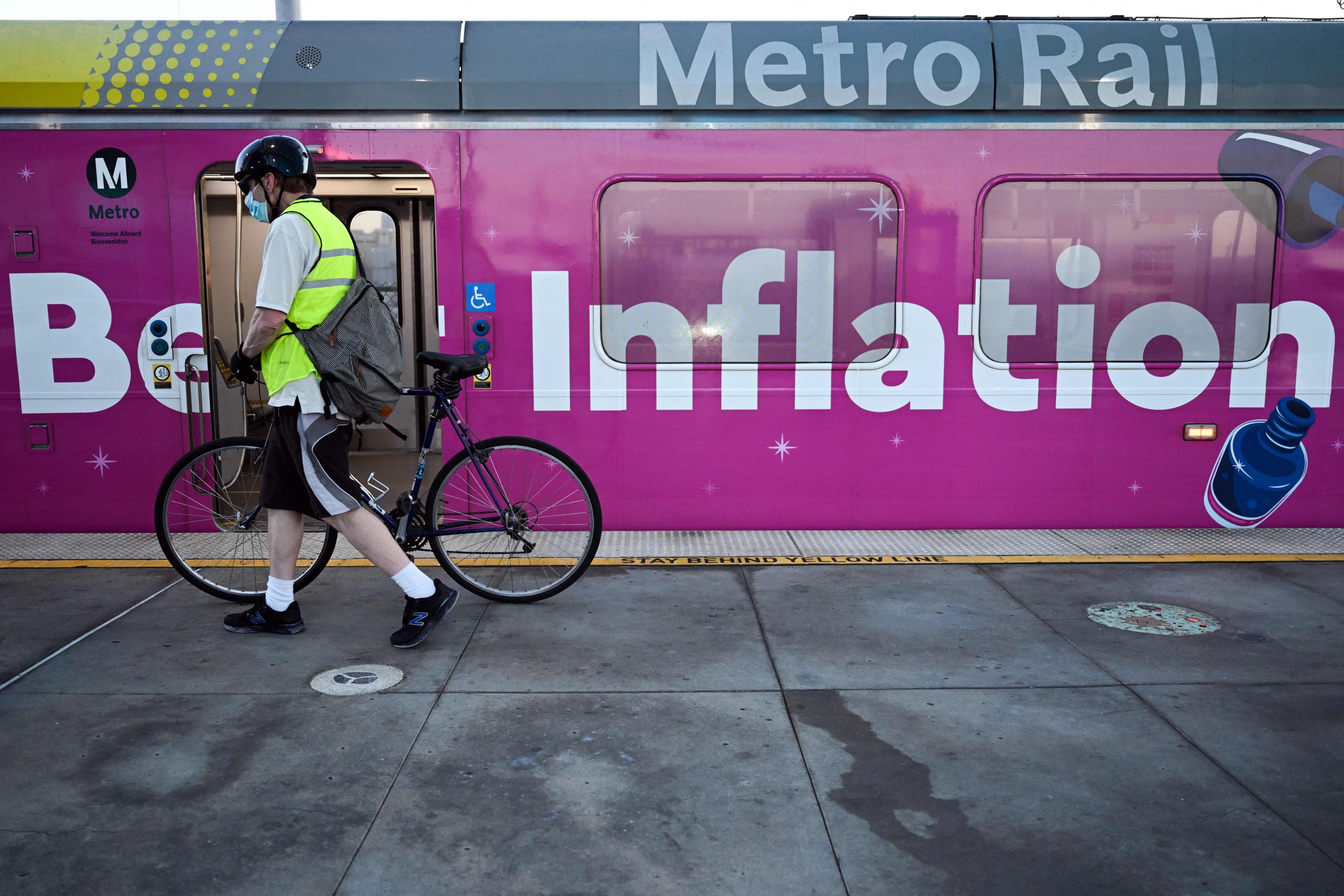 A cyclist pushes a bicycle past a Metro green line light rail train wrapped with a “Beat Inflation” advertisement for the 99 Cents Only Stores, in Redondo Beach, California. Photo: AFP