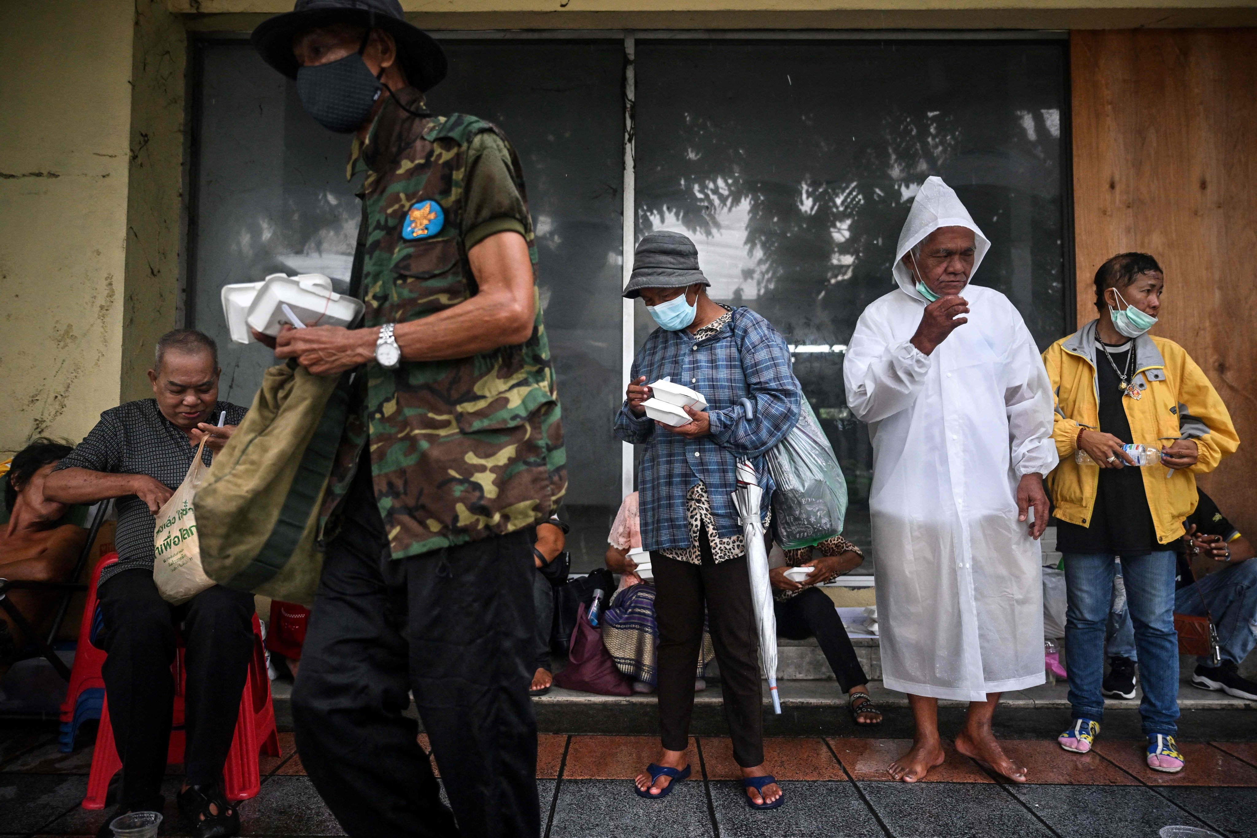 People shelter from the rain after receiving meals from volunteers from Bangkok Community Help Foundation in Bangkok on September 13. Soaring energy prices are driving inflation in economies like Thailand, where the energy-intensive transport category has a big weight in the consumption basket. Photo: AFP 